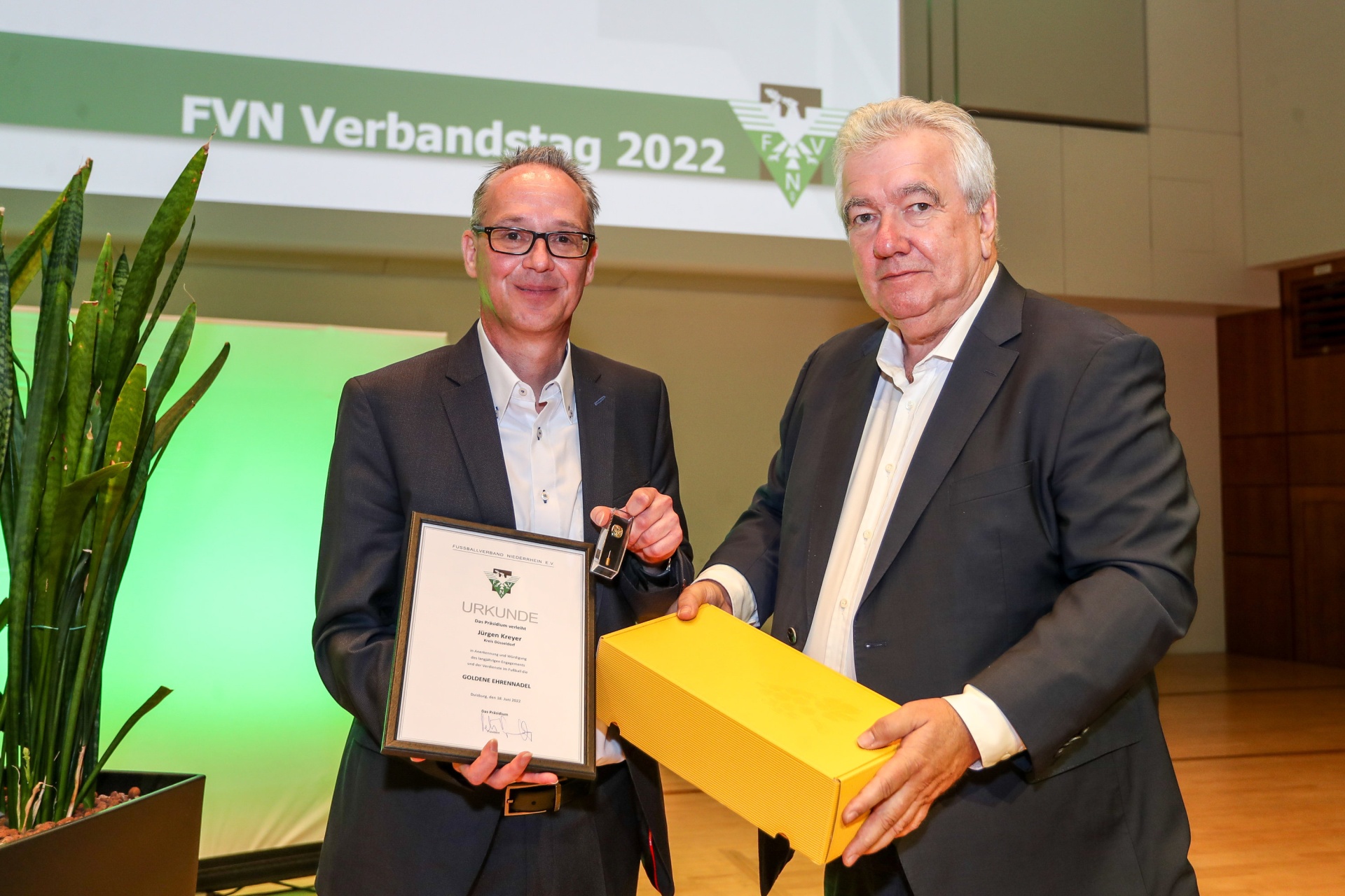 [{"clang_id":1,"value":"Zwei Männer stehen auf einer Bühne vor einem Banner mit dem Schriftzug \"FVN Verbandstag 2022\". Der linke Mann übergibt dem rechten eine Urkunde und eine kleine Schachtel."}]