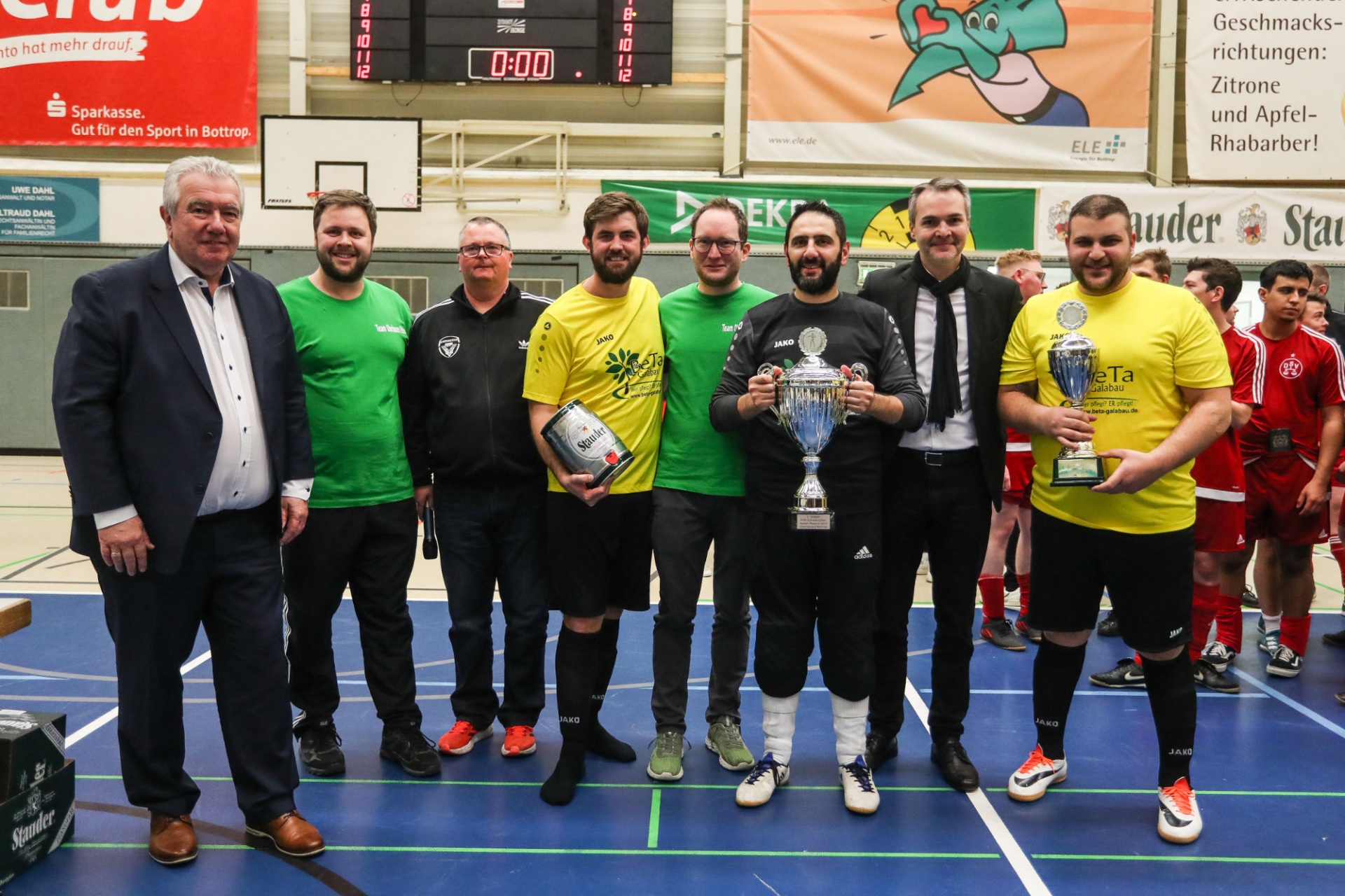 [{"clang_id":1,"value":"Gruppe von Männern in Sportkleidung, einige mit Trophäen, posieren in einer Sporthalle. Im Hintergrund Werbung und eine Anzeigetafel."}]