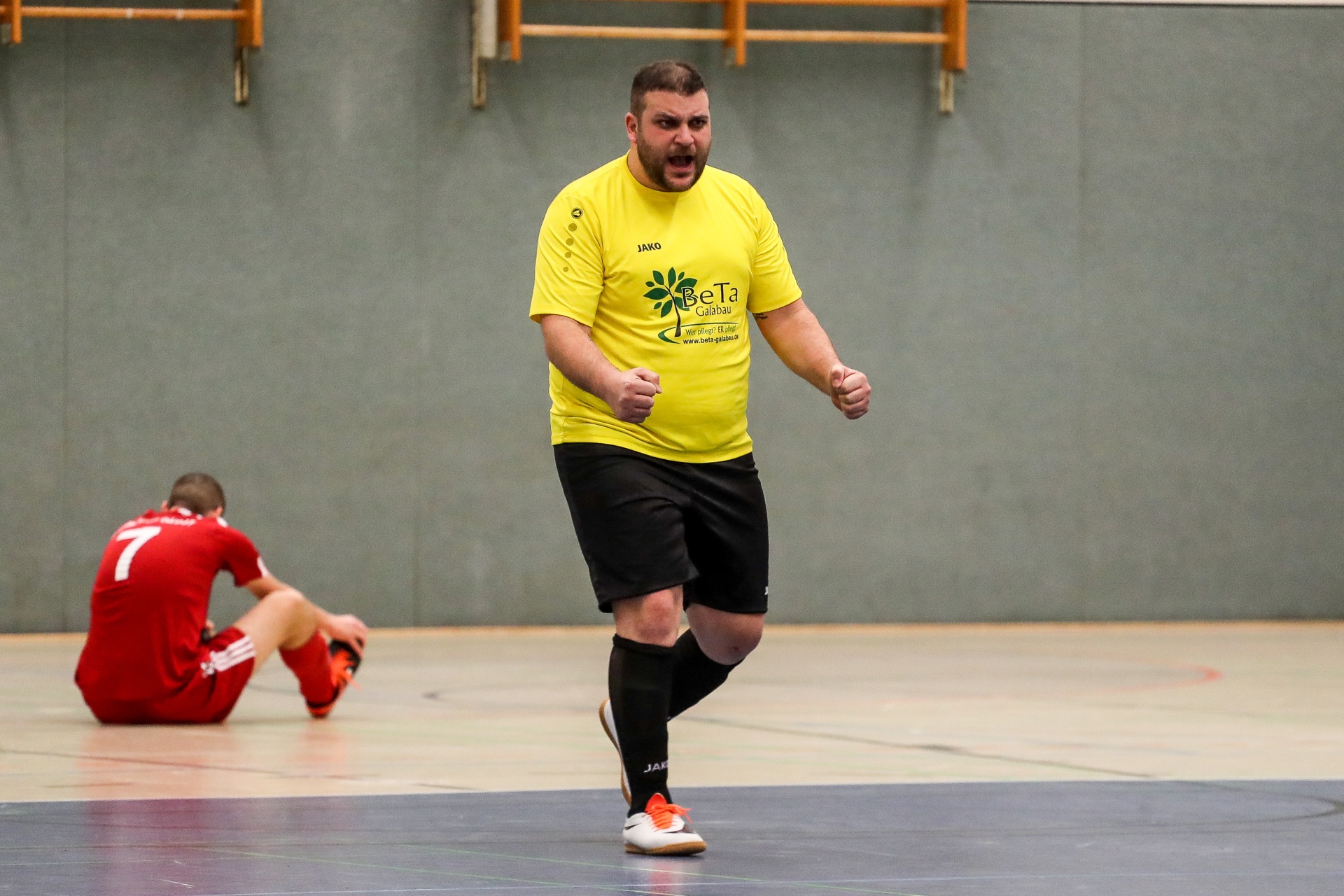 [{"clang_id":1,"value":"Handballspieler in gelbem Trikot und kurzer Hose jubelt auf Hallenboden. Im Hintergrund ein Spieler in roten Shorts, der auf dem Boden sitzt."}]