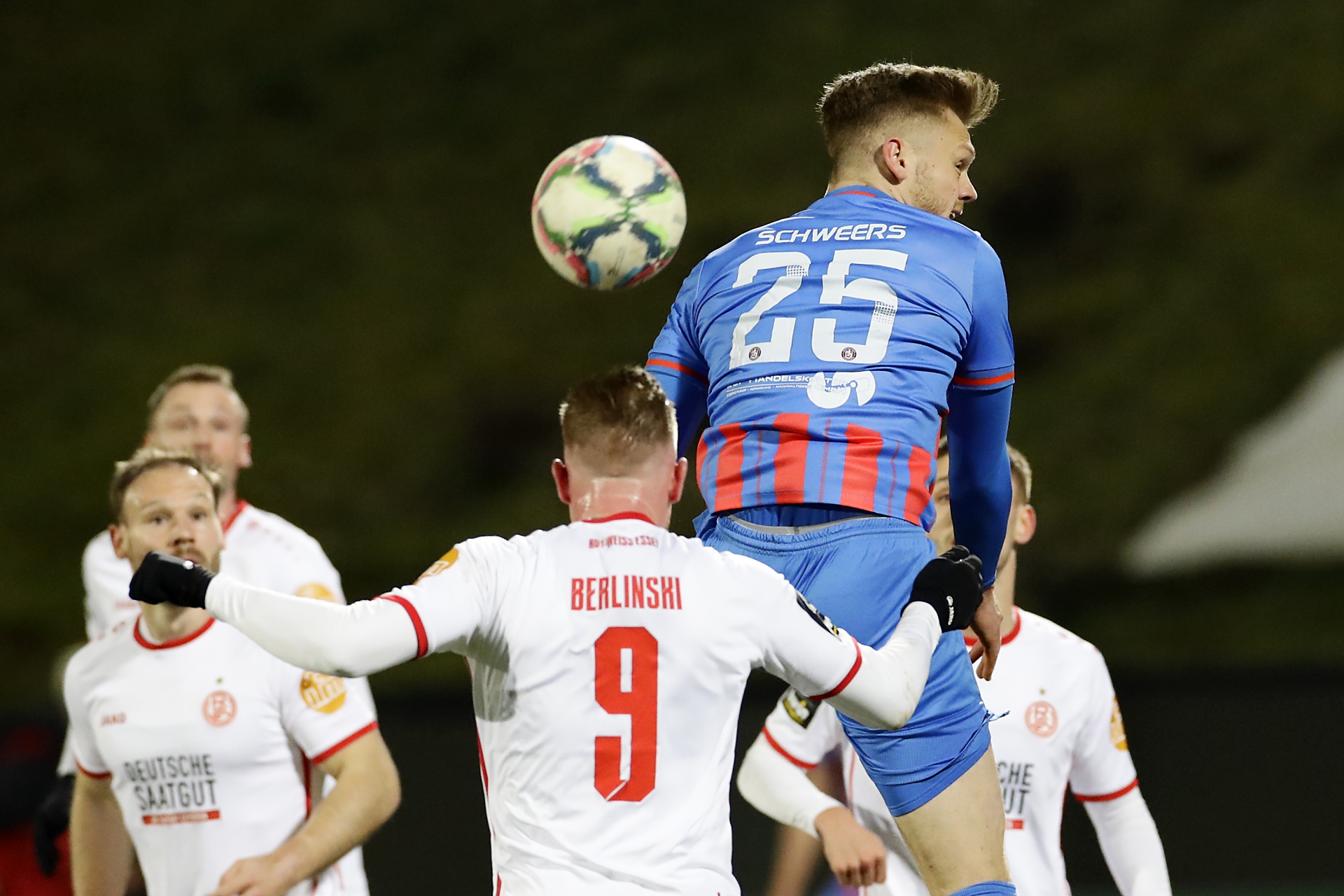 [{"clang_id":1,"value":"Fußballspieler springt mit hoch erhobenem Kopf, um Ball per Kopf zu spielen. Im Hintergrund weitere Spieler in weißen und roten Trikots."}]