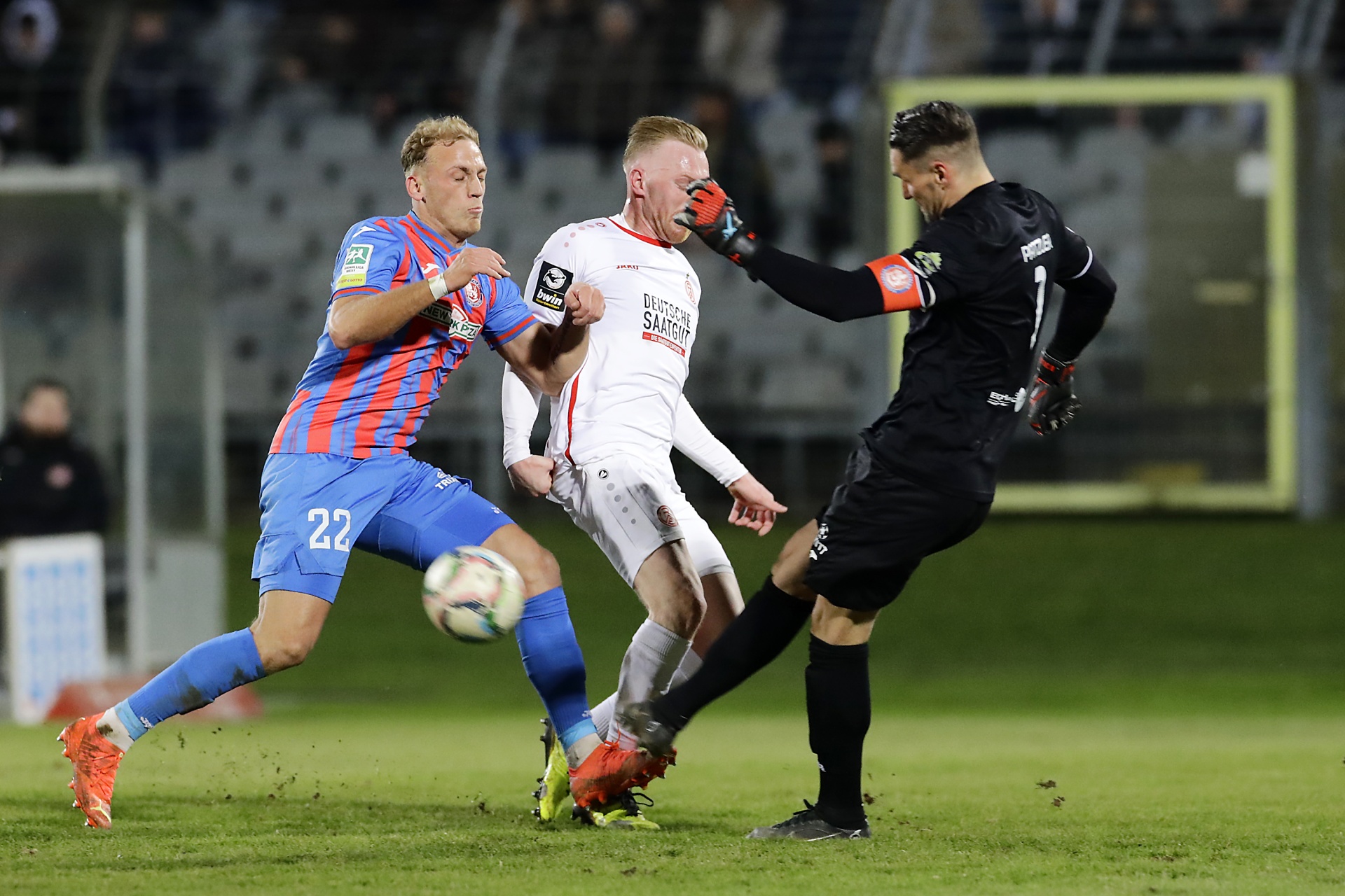 [{"clang_id":1,"value":"Fußballspiel: Spieler mit Ball in Nahheit zum Torwart. Links ein Spieler mit blauem Trikot und Nummer 22, in der Mitte ein Spieler mit weißem Trikot, rechts der Torwart in schwarzer Ausrüstung."}]