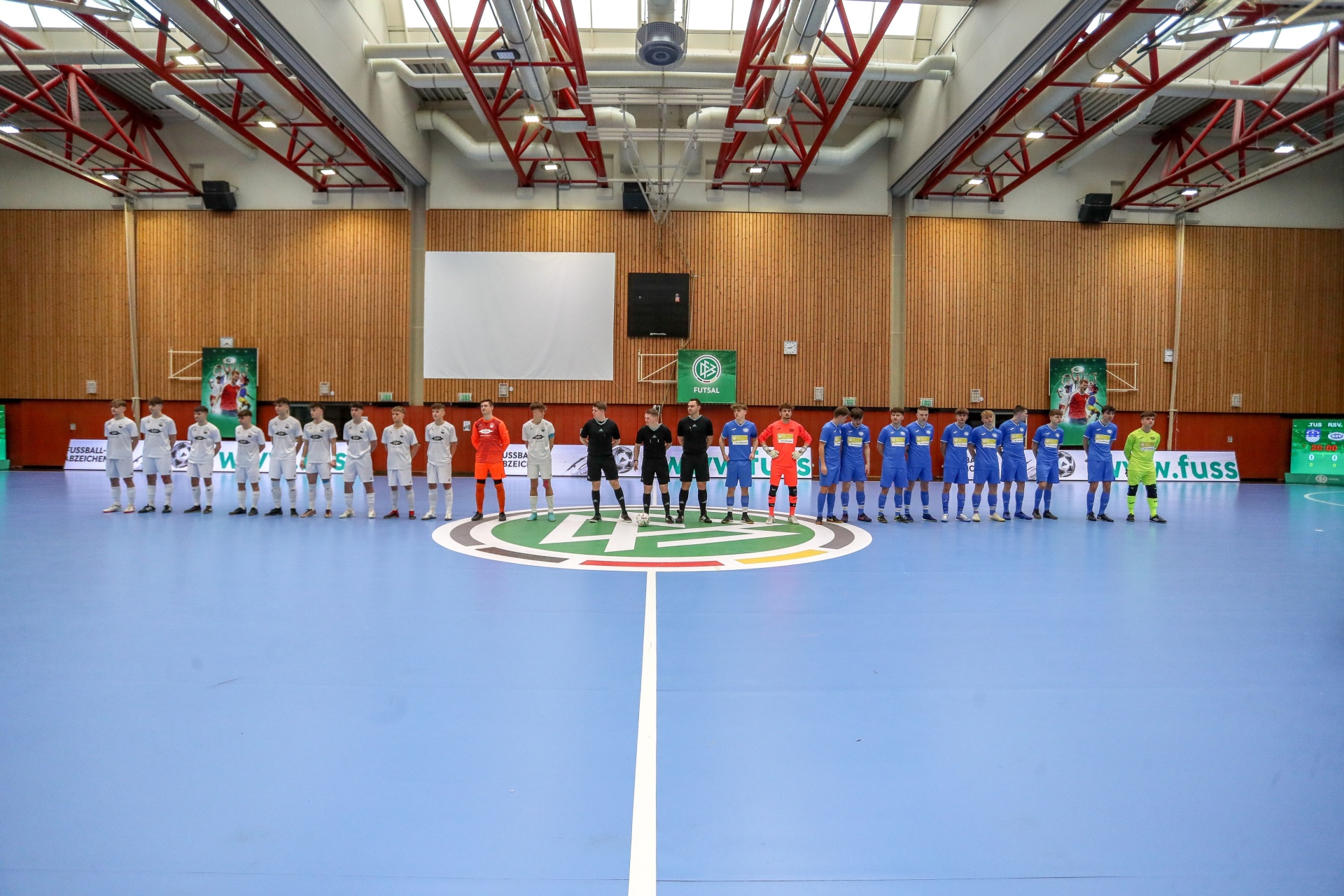 [{"clang_id":1,"value":"Futsal-Mannschaften stehen sich in einer Sporthalle gegenüber. Zwei Teams in dunklen bzw. hellen Trikots, dazwischen Schiedsrichter."}]