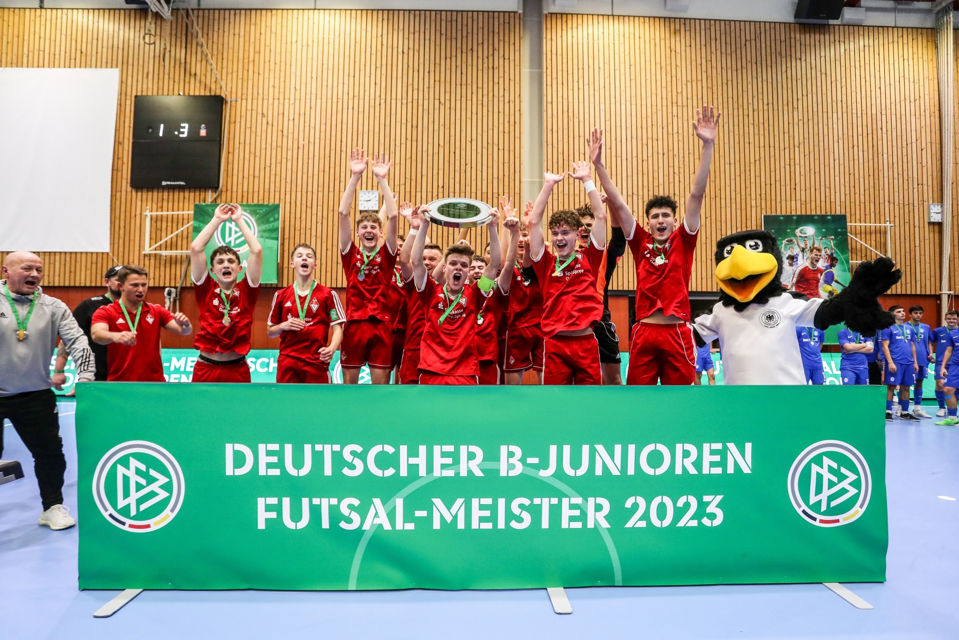 [{"clang_id":1,"value":"Futsal-Mannschaft mit Pokal. Schriftzug \"Deutscher B-Junioren Futsal-Meister 2023\" auf grünem Banner. Hintergrund: Sporthalle mit Zuschauern."}]