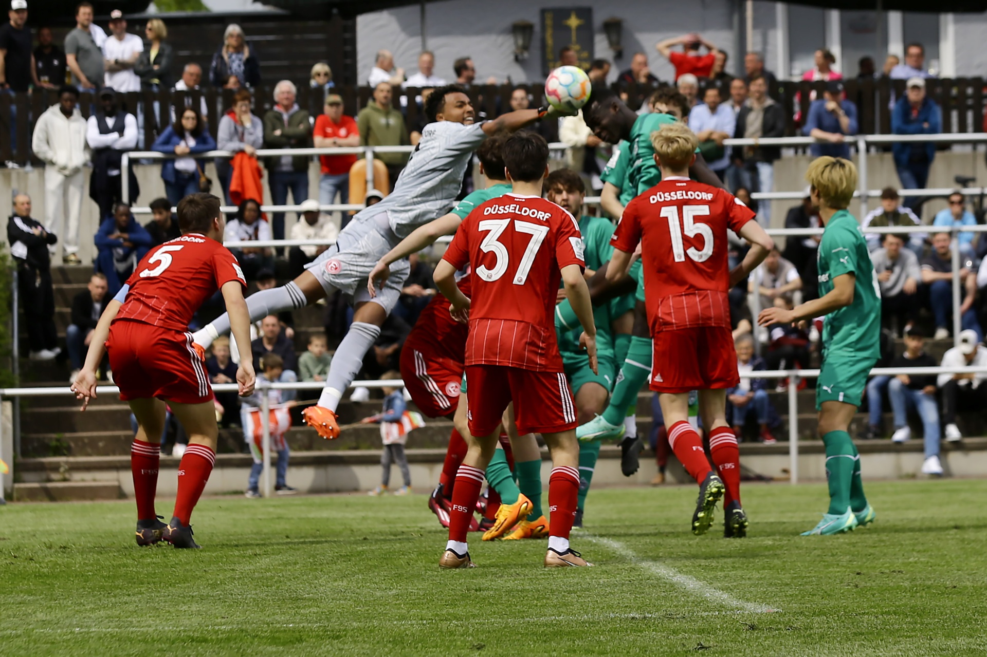 [{"clang_id":1,"value":"Fußballspiel: Spieler in roten und grünen Trikots kämpfen um den Ball. Ein Spieler springt hoch, um den Ball zu köpfen. Im Hintergrund Zuschauer auf Tribünen."}]