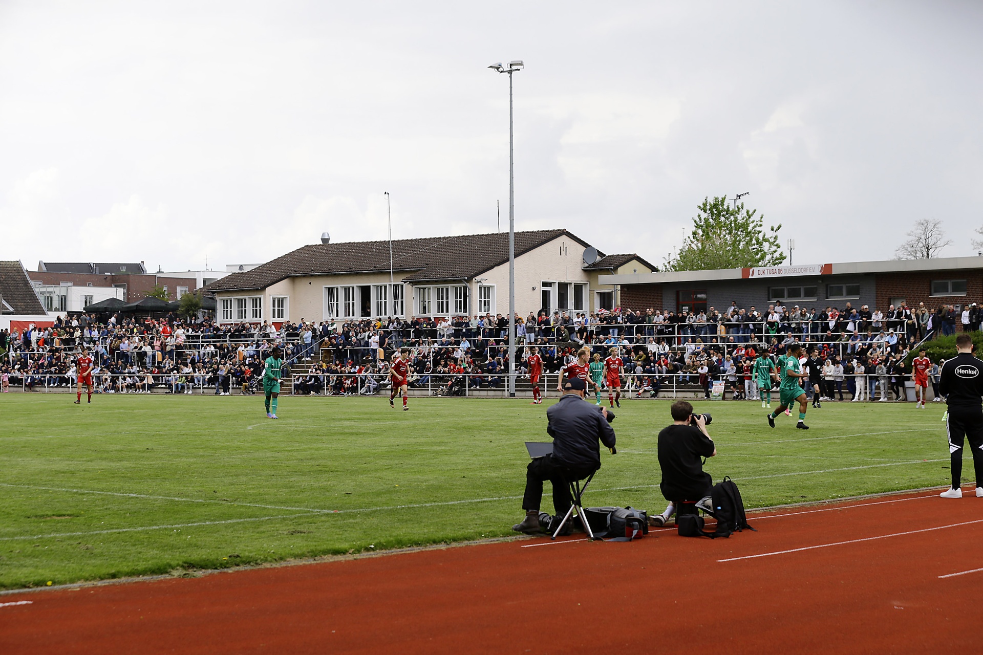 [{"clang_id":1,"value":"Fußballspiel im Stadion. Rasenplatz mit rot laufbahn. Zuschauerreihen im Hintergrund, Gebäude. Zwei Fotografen am Spielfeldrand."}]