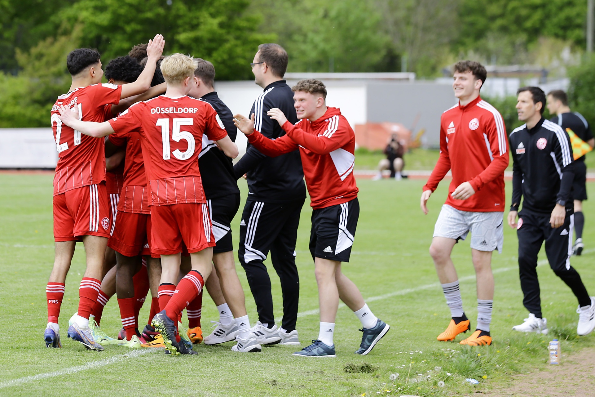 [{"clang_id":1,"value":"Fußballspieler in roten Trikots feiern auf grünem Rasen. Im Hintergrund stehen weitere Spieler und Trainer in Trainingskleidung."}]