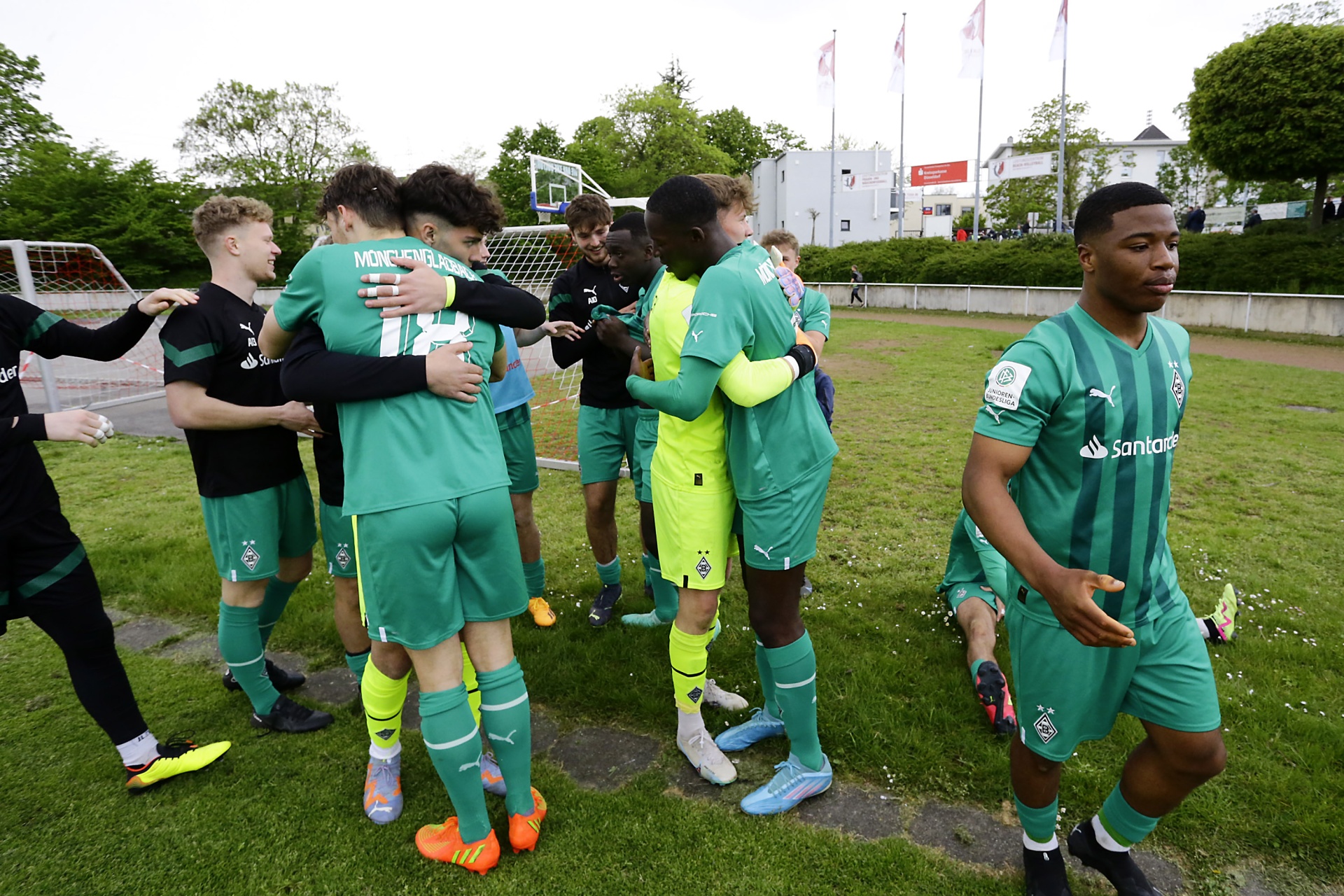 [{"clang_id":1,"value":"Fußballspieler in grünen Trikots umarmen und feiern auf einem Rasenplatz. Im Hintergrund Gebäude und Bäume."}]