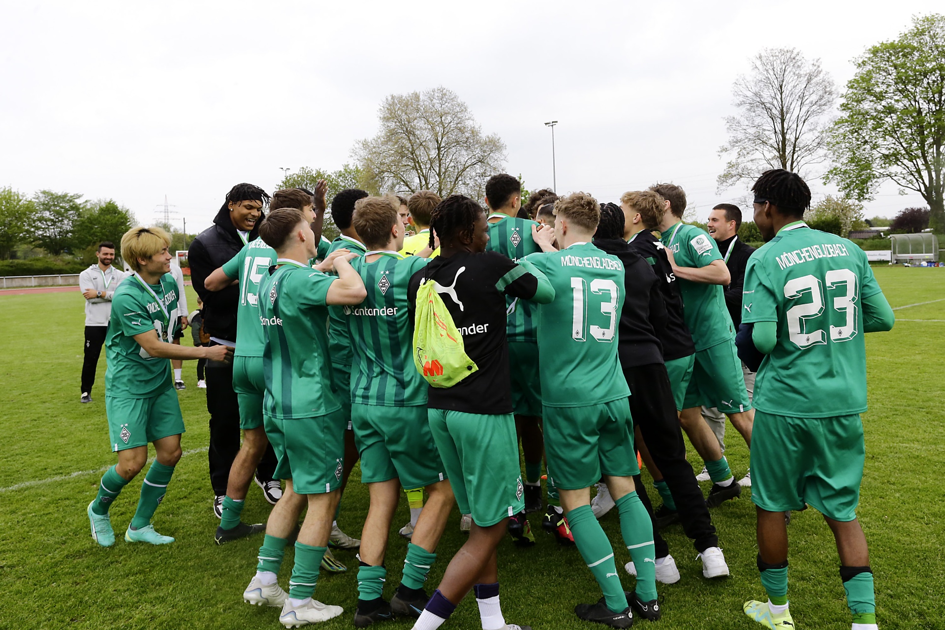 [{"clang_id":1,"value":"Fußballmannschaft in grünen Trikots feiert Sieg auf dem Rasen. Spieler umarmen sich und jubeln. Im Hintergrund Bäume und eine Zuschauertribüne."}]