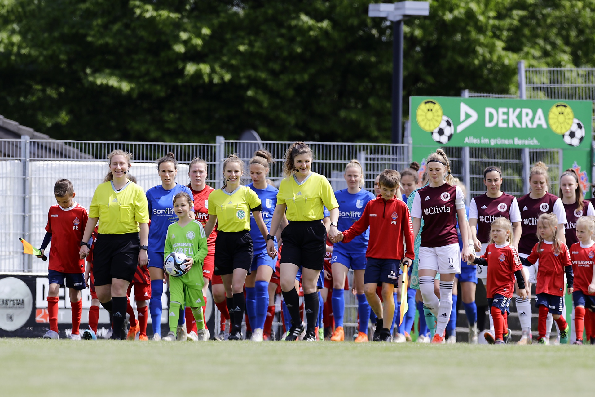 [{"clang_id":1,"value":"Fußballspiel: Zwei Frauenteams in rot-schwarzer bzw. blau-schwarzer Ausrüstung stehen sich auf einem Rasenplatz gegenüber, begleitet von Schiedsrichterinnen. Im Hintergrund eine Zuschauertribüne."}]