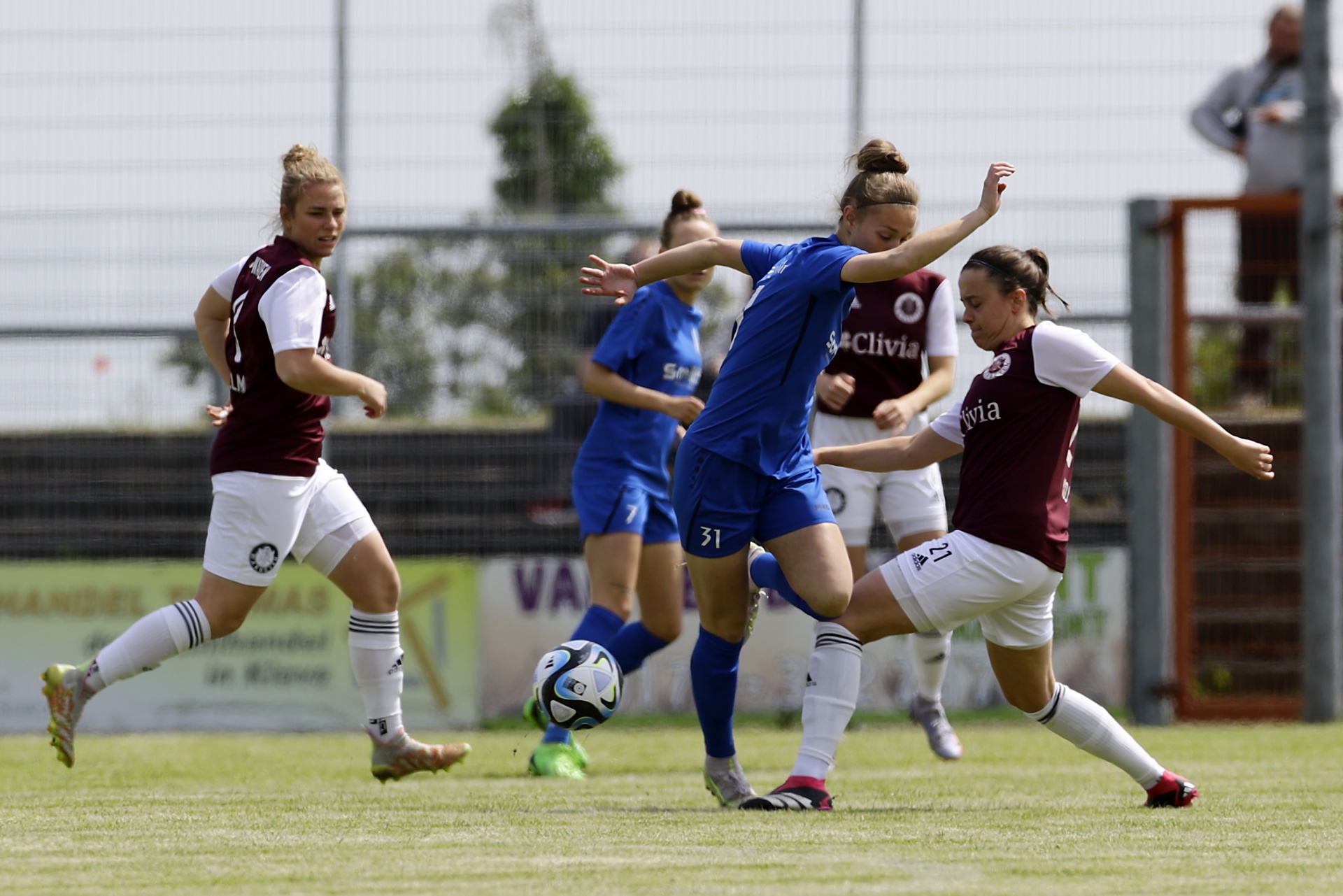 [{"clang_id":1,"value":"Fußballspiel: Drei Spielerinnen kämpfen um den Ball auf grünem Rasen. Links rote Trikots, Mitte blaues Trikot mit Nummer 31, rechts rotes Trikot mit Nummer 21."}]