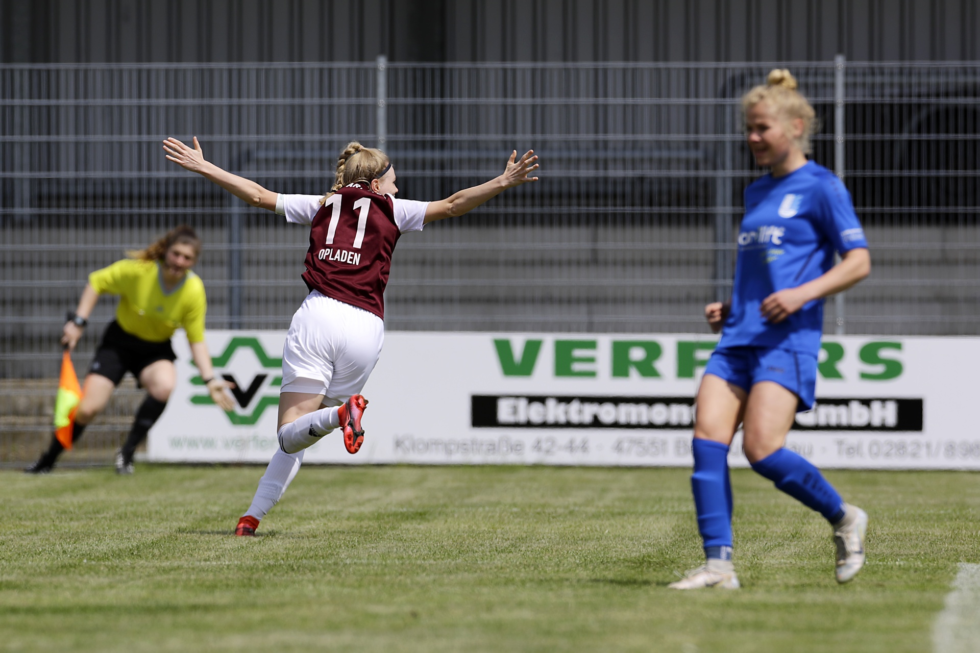 [{"clang_id":1,"value":"Fußballspiel: Spielerin mit Nummer 11 in Rot/Weiß jubelt, eine Gegenspielerin in Blau läuft im Hintergrund. Im Hintergrund eine Werbetafel und ein Zaun."}]