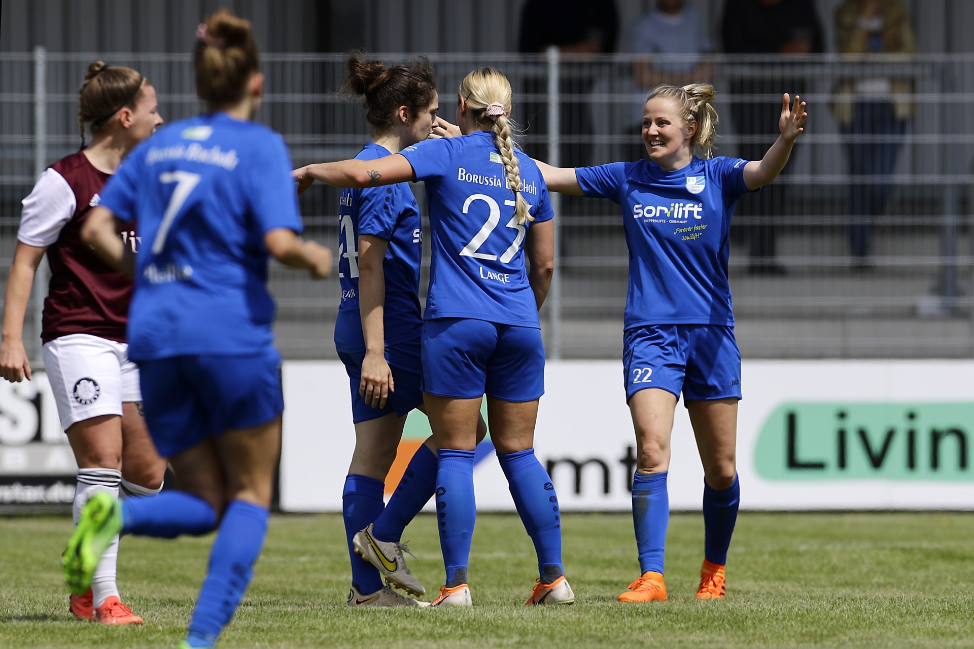 [{"clang_id":1,"value":"Fußballspiel: Vier Spielerinnen in blauen Trikots feiern mit erhobenen Armen, umringt von Spielerinnen in roten und weißen Trikots auf einem Fußballfeld."}]