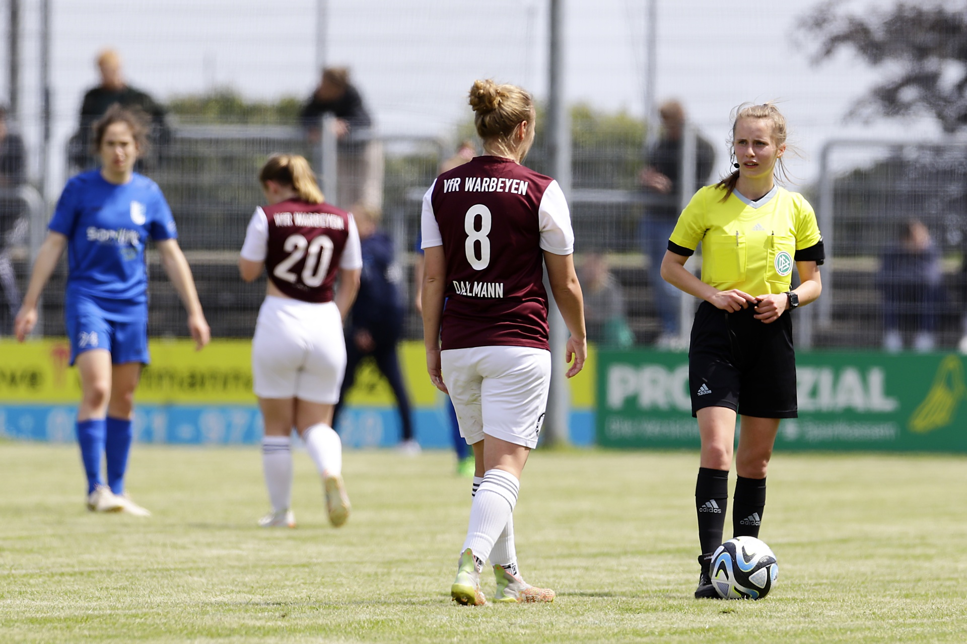 [{"clang_id":1,"value":"Fußballspiel: Drei Spielerinnen und eine Schiedsrichterin auf grünem Rasen. Eine Spielerin trägt blaues Trikot, eine rote mit Nummer 8, die Schiedsrichterin schwarz-gelbes Outfit."}]