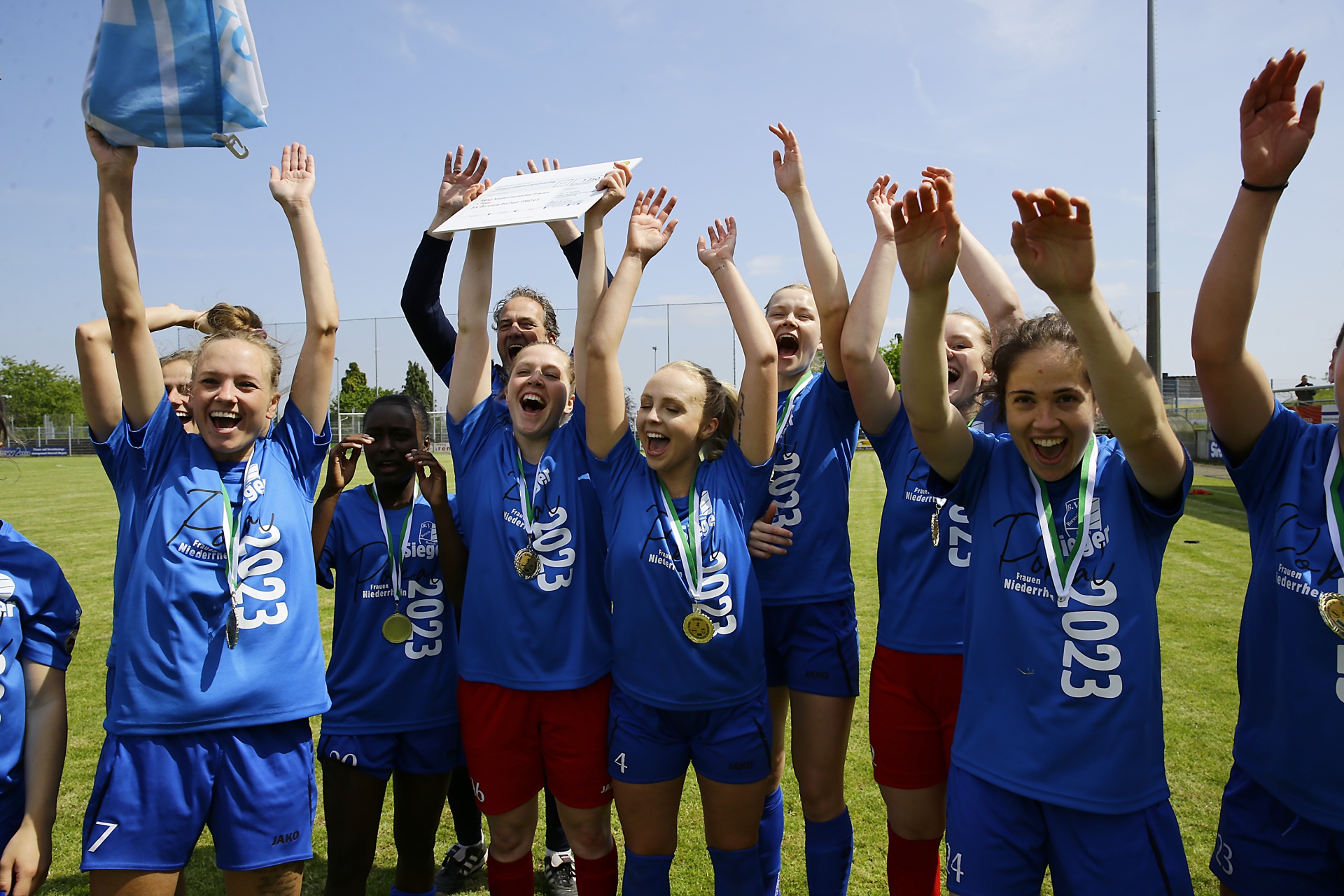 [{"clang_id":1,"value":"Fußballmannschaft mit blauen Trikots und Shorts feiert Sieg. Spielerinnen halten Pokal und Medaillen in die Höhe, jubeln auf einem Rasenplatz."}]