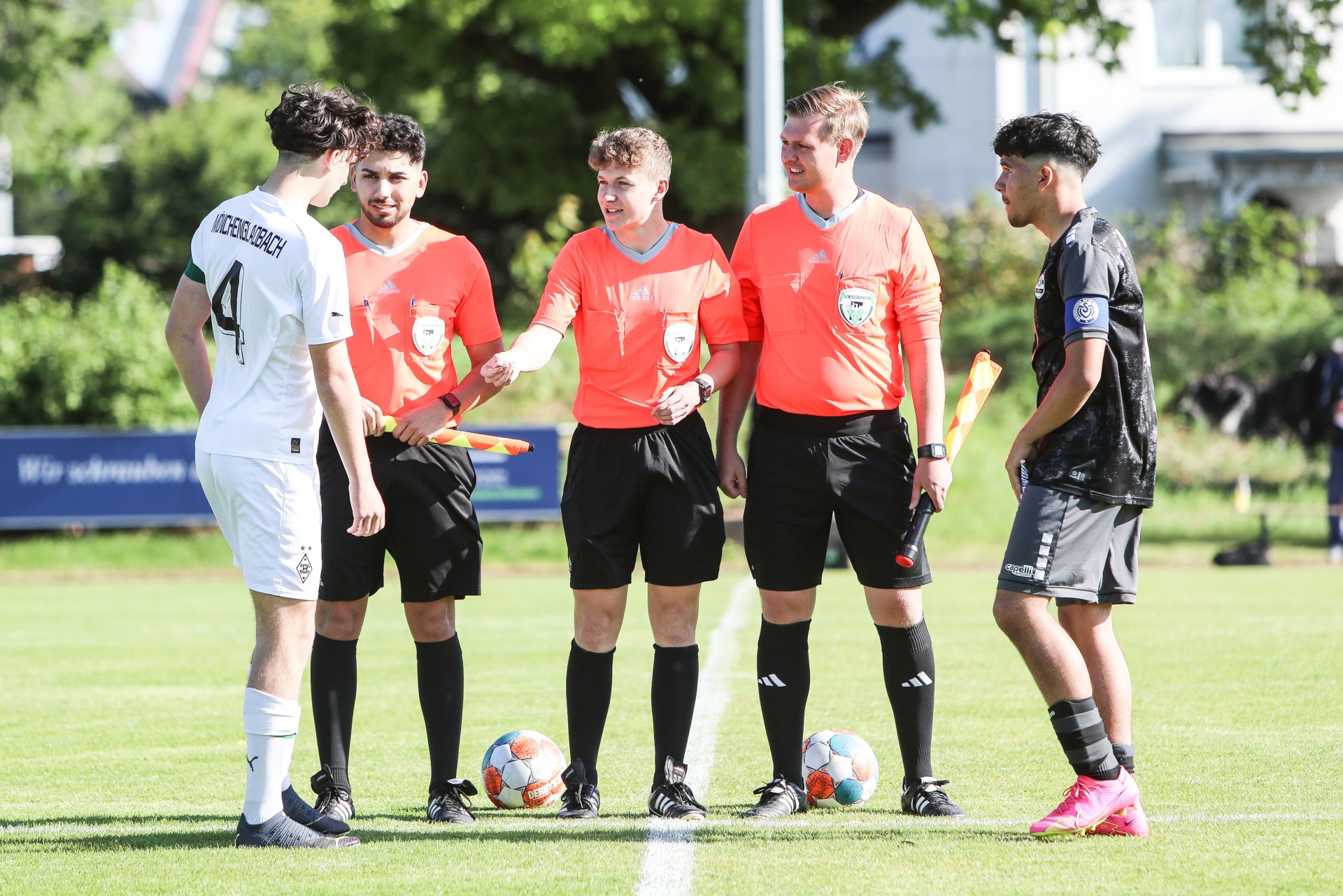 [{"clang_id":1,"value":"Fußballspiel: Zwei Spieler mit gelben und schwarzen Trikots stehen mit drei Schiedsrichtern in orangefarbenen Shirts auf dem Rasen. Vor ihnen liegen Fußbälle."}]