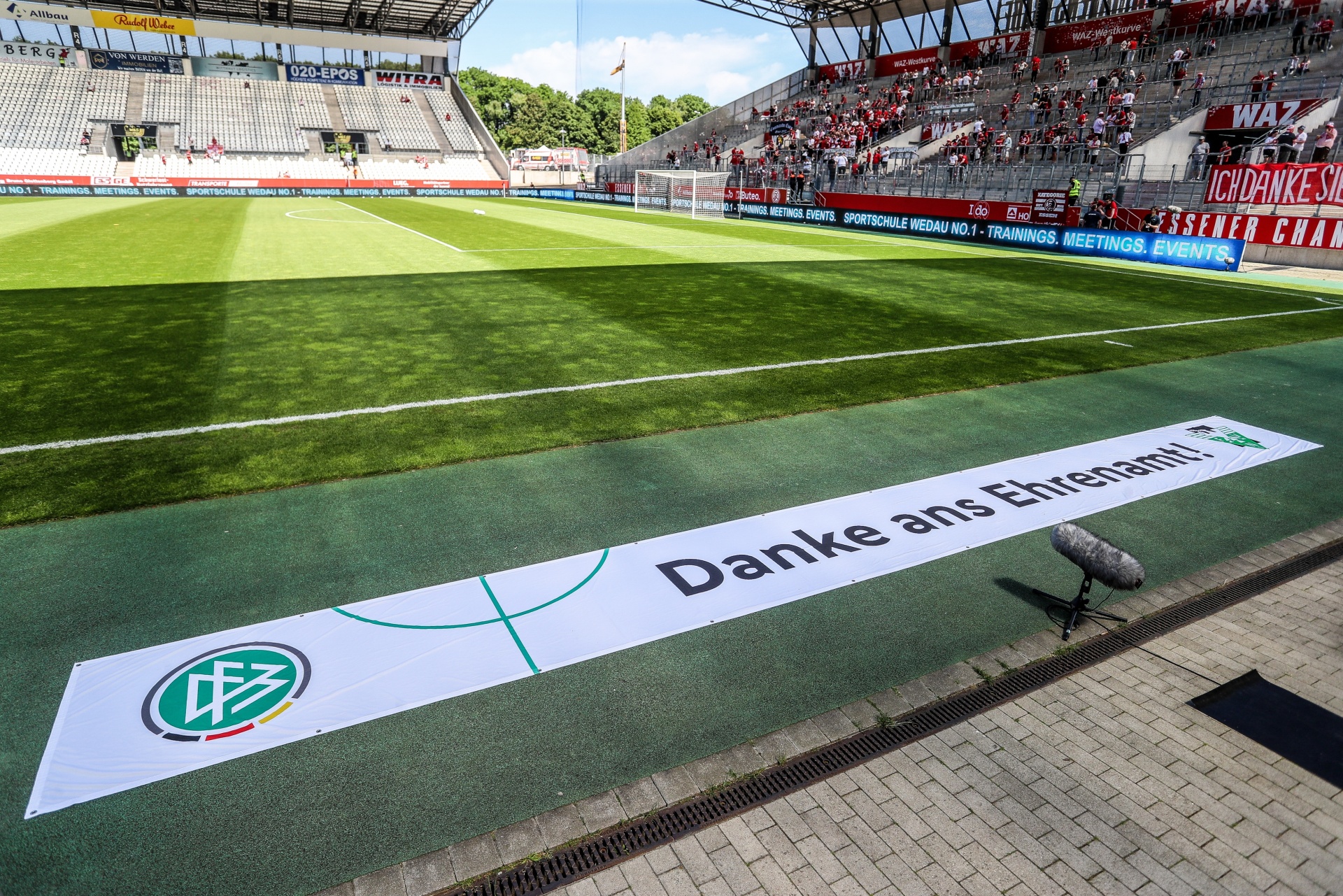 [{"clang_id":1,"value":"Fußballstadion mit Rasenplatz. Im Vordergrund Banner mit Aufschrift \"Danke ans Ehrenamt!\" und Vereinslogo. Zuschauerreihen im Hintergrund."}]