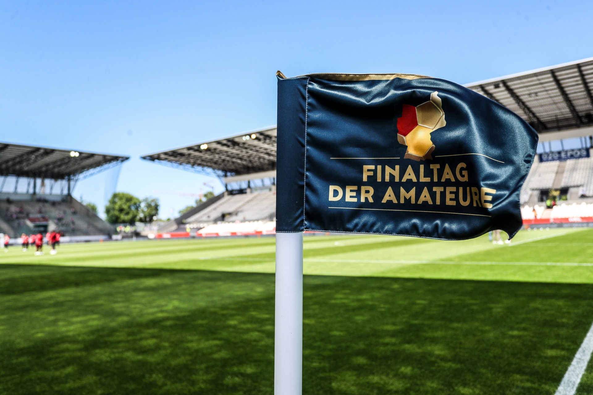 [{"clang_id":1,"value":"Fußballstadion mit Fahne im Vordergrund. Auf der Fahne steht \"Finaltag der Amateure\" in weißer Schrift auf dunkelblauem Grund. Rasen und Zuschauerränge im Hintergrund."}]
