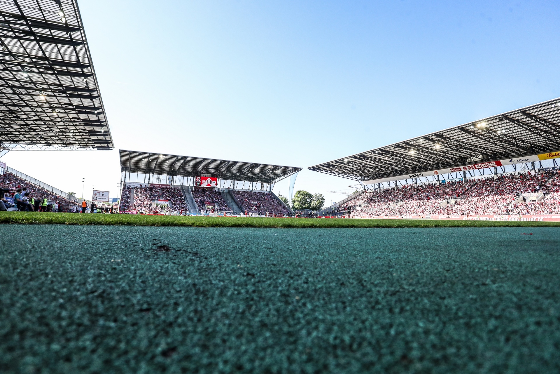[{"clang_id":1,"value":"Fußballstadion mit Rasenplatz aus der Sicht eines Spielers. Zuschauerreihen und Dachkonstruktionen sind sichtbar. Helles Tageslicht, blauer Himmel."}]