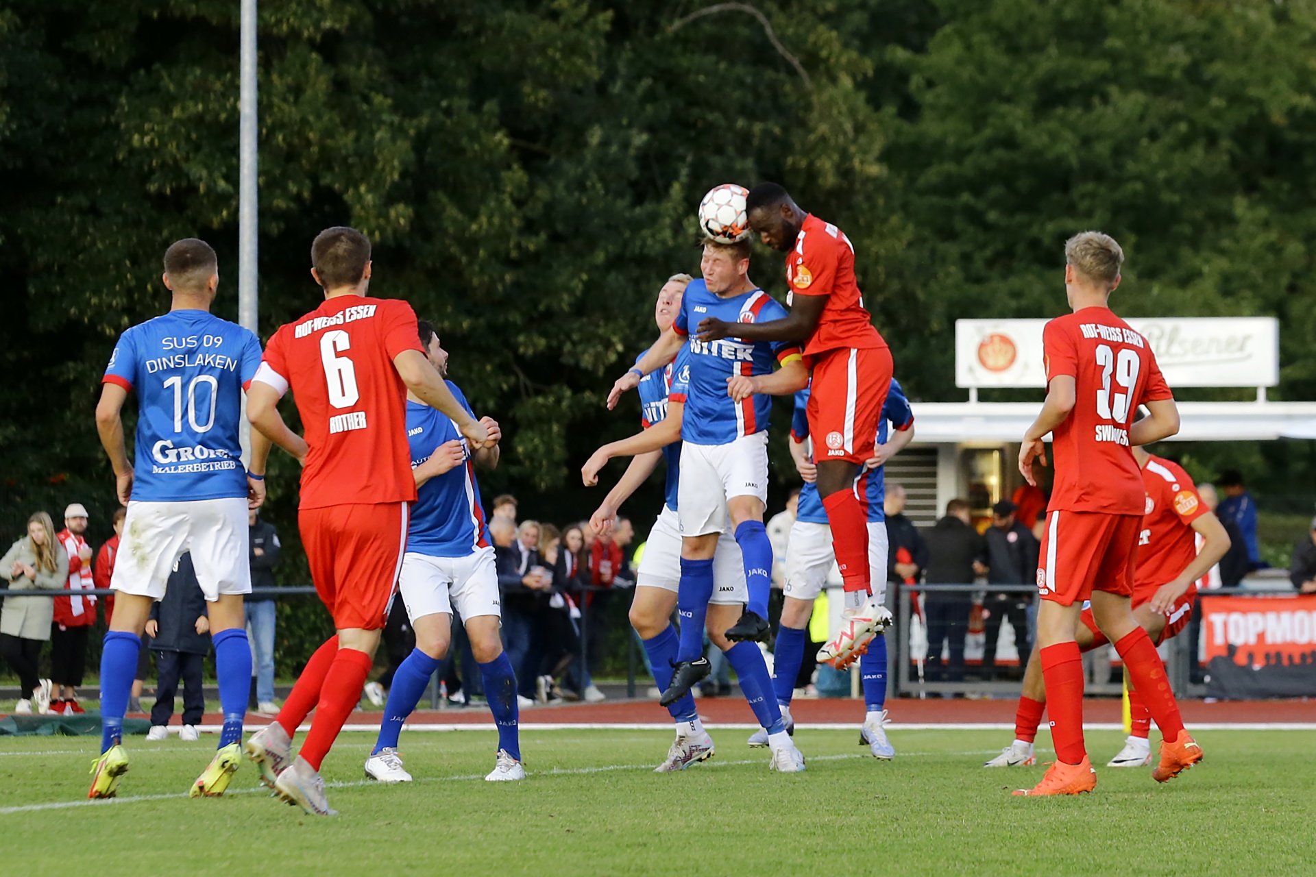 [{"clang_id":1,"value":"Fußballspiel: Spieler in rot und blau kämpfen um den Ball per Kopfball im Strafraum. Zuschauer im Hintergrund."}]