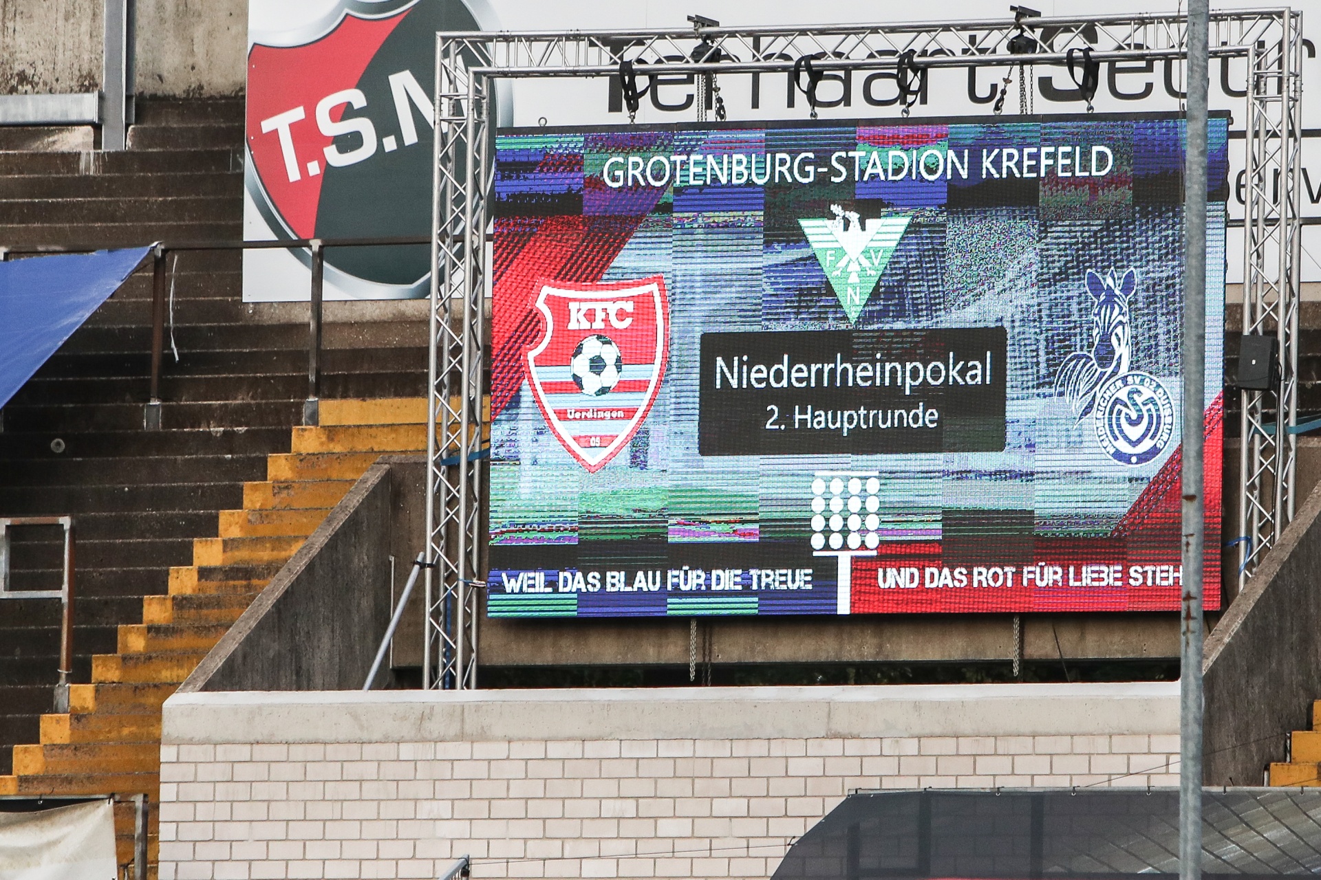 [{"clang_id":1,"value":"Fußballstadion-Videoleinwand zeigt KFC Uerdingen Logo und \"Niederrheinpokal 2. Hauptrunde\". Im Hintergrund Stadiontribüne und Zaun."}]