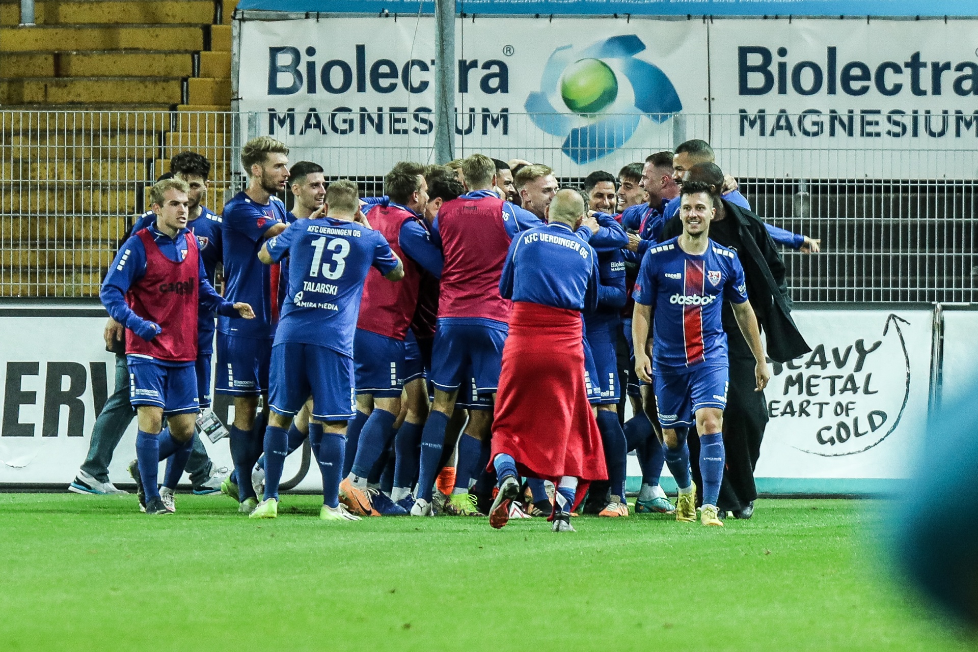 [{"clang_id":1,"value":"Fußballspieler in rot-blauem und rot-weißem Trikot feiern auf grünem Rasen. Im Hintergrund eine Werbebande mit dem Schriftzug \"Biolectra Magnesium\"."}]