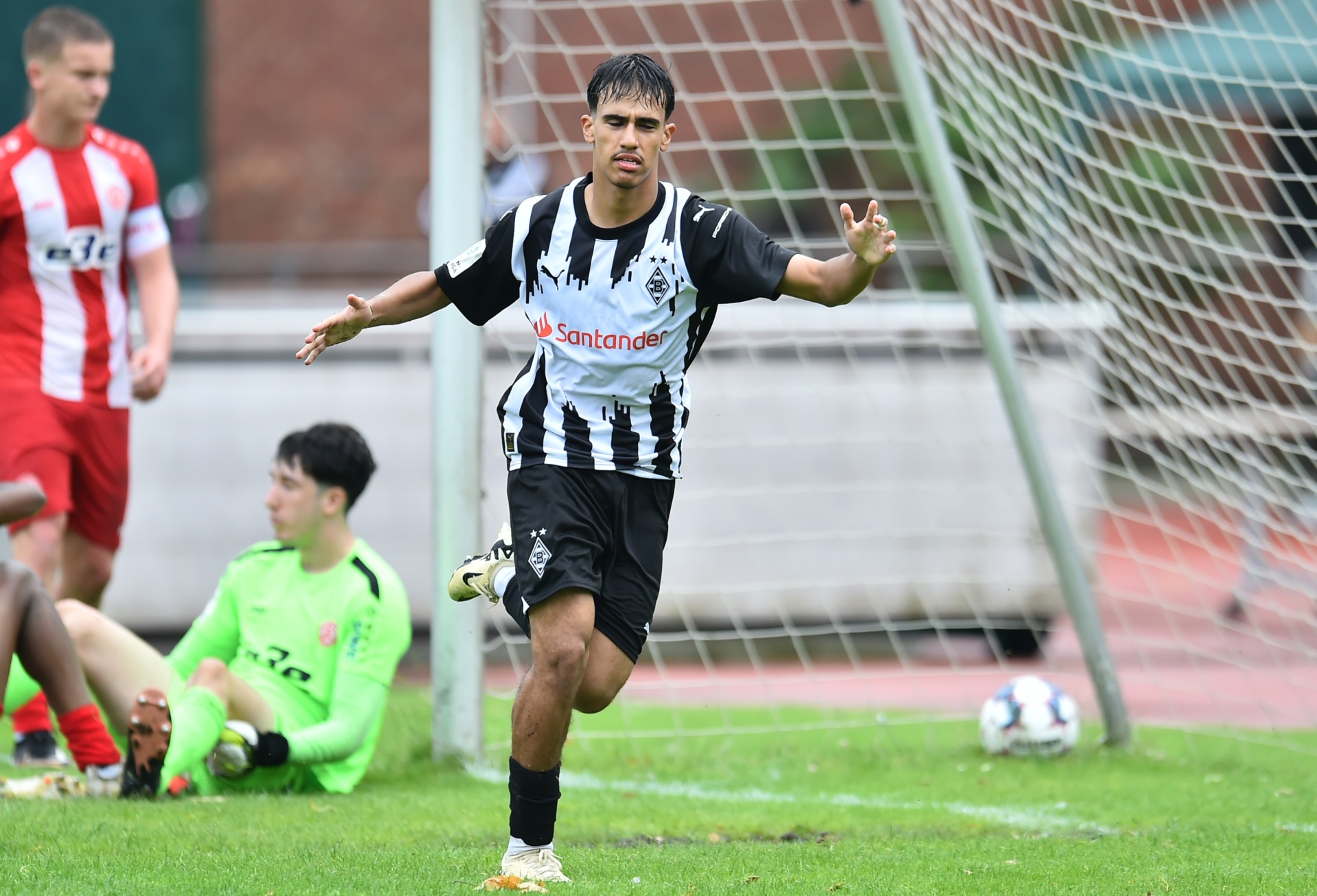 [{"clang_id":1,"value":"Fußballspieler in schwarz-weißem Trikot feiert Tor auf grünem Rasen. Im Hintergrund weitere Spieler und ein Fußballtor."}]