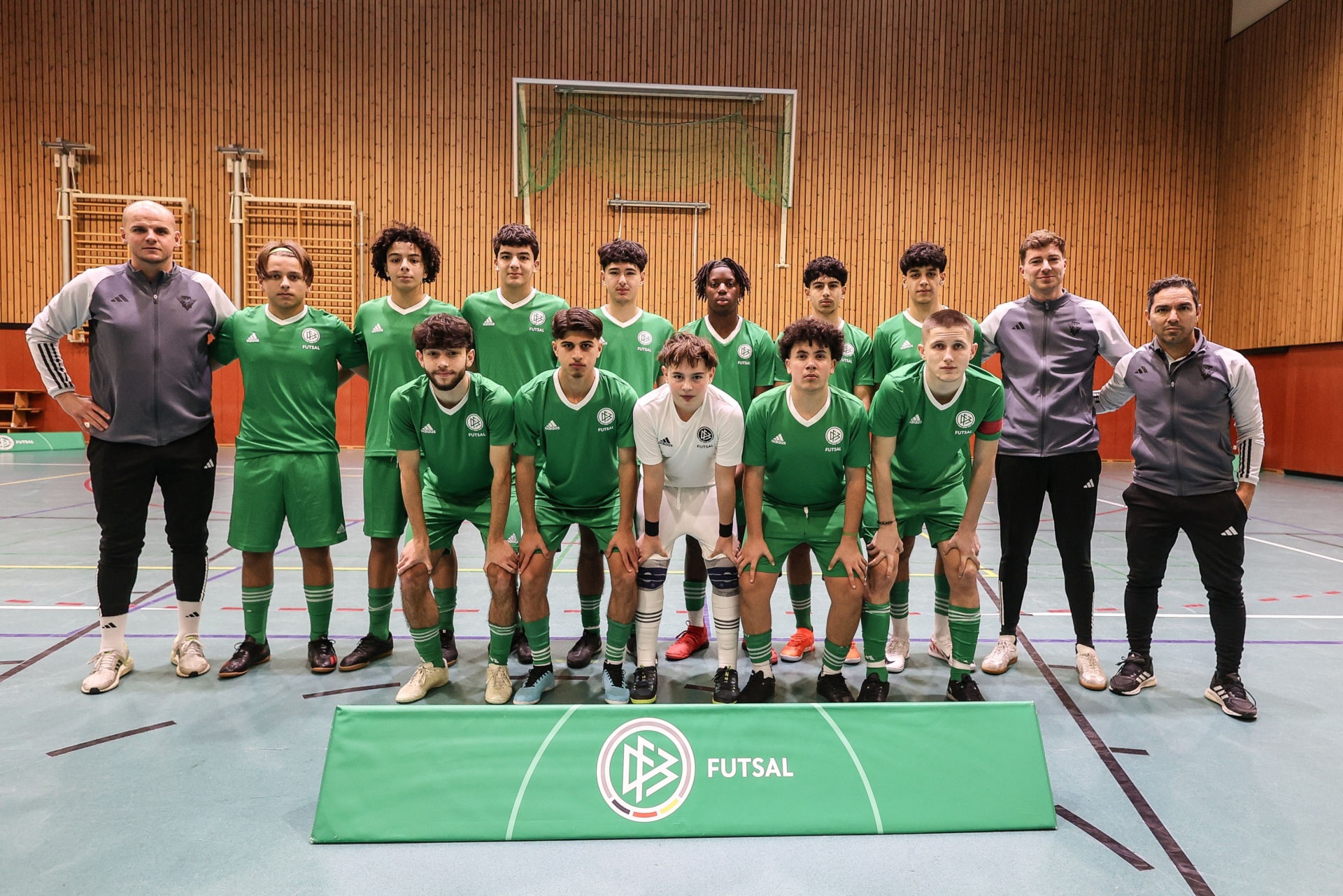 [{"clang_id":1,"value":"Futsalmannschaft in grünen Trikots mit Trainern, stehend vor einer Holzwand in einer Sporthalle. Logo \"Futsal\" im Vordergrund."}]