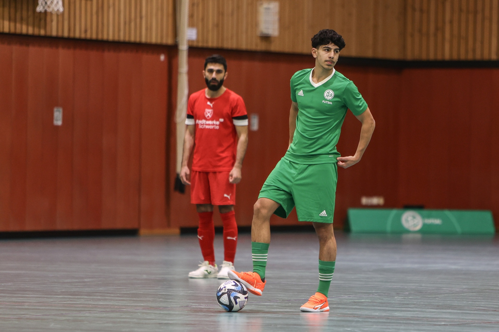 [{"clang_id":1,"value":"Zwei Fußballspieler in einem Turnhalle. Einer trägt grünes Trikot, der andere rotes Trikot. Der vordere Spieler dribbelt einen Fußball."}]
