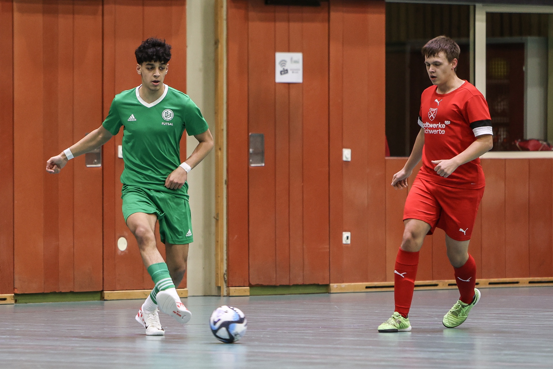 [{"clang_id":1,"value":"Zwei Fussballspieler in Sporthalle. Links Spieler in grünem Trikot, rechts in rotem Trikot. Beide mit Fussball am Boden."}]