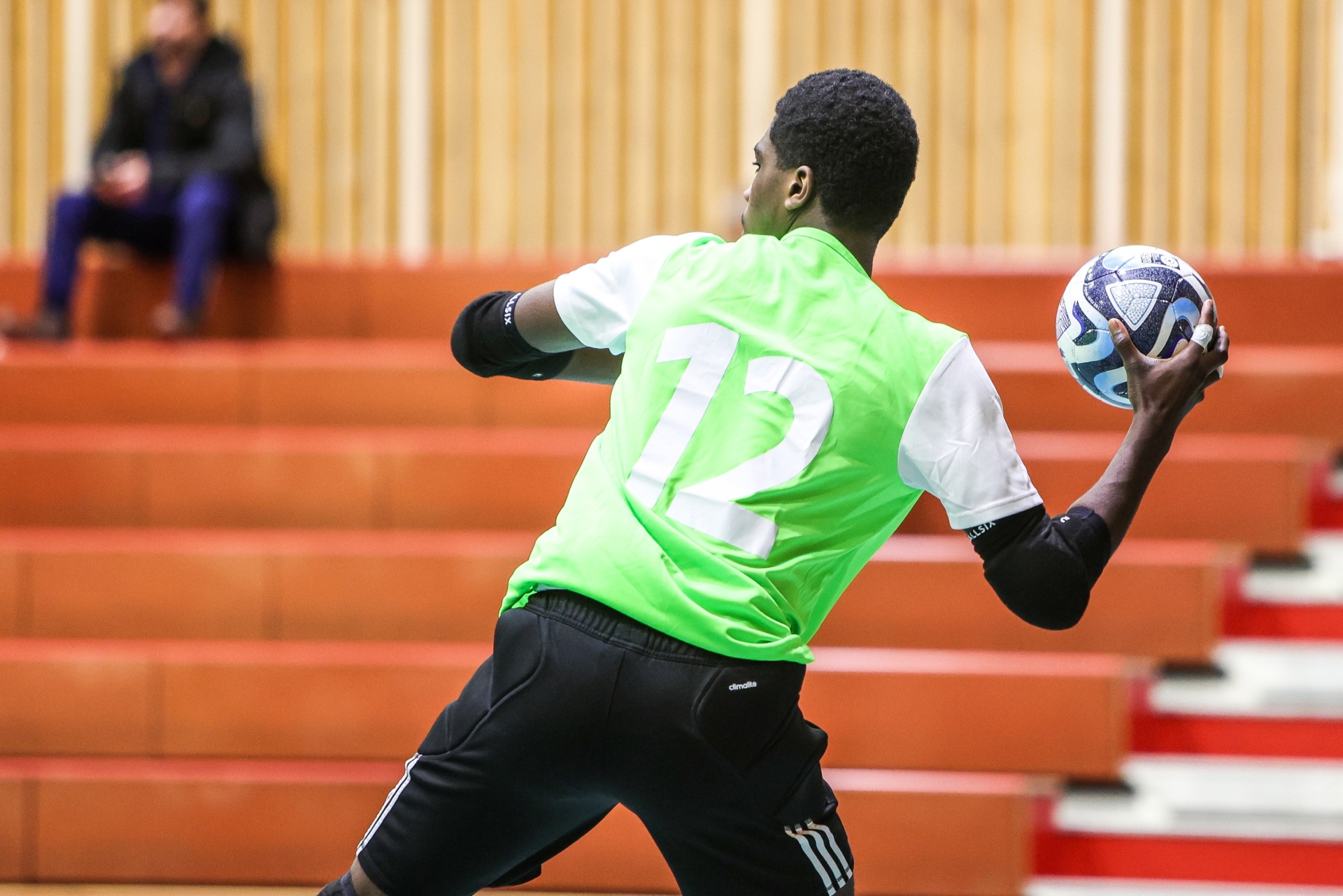 [{"clang_id":1,"value":"Junger Fußballspieler mit grünem Trainingsleibchen und schwarzer Hose wirft einen Ball seitlich. Im Hintergrund Zuschauerränge."}]