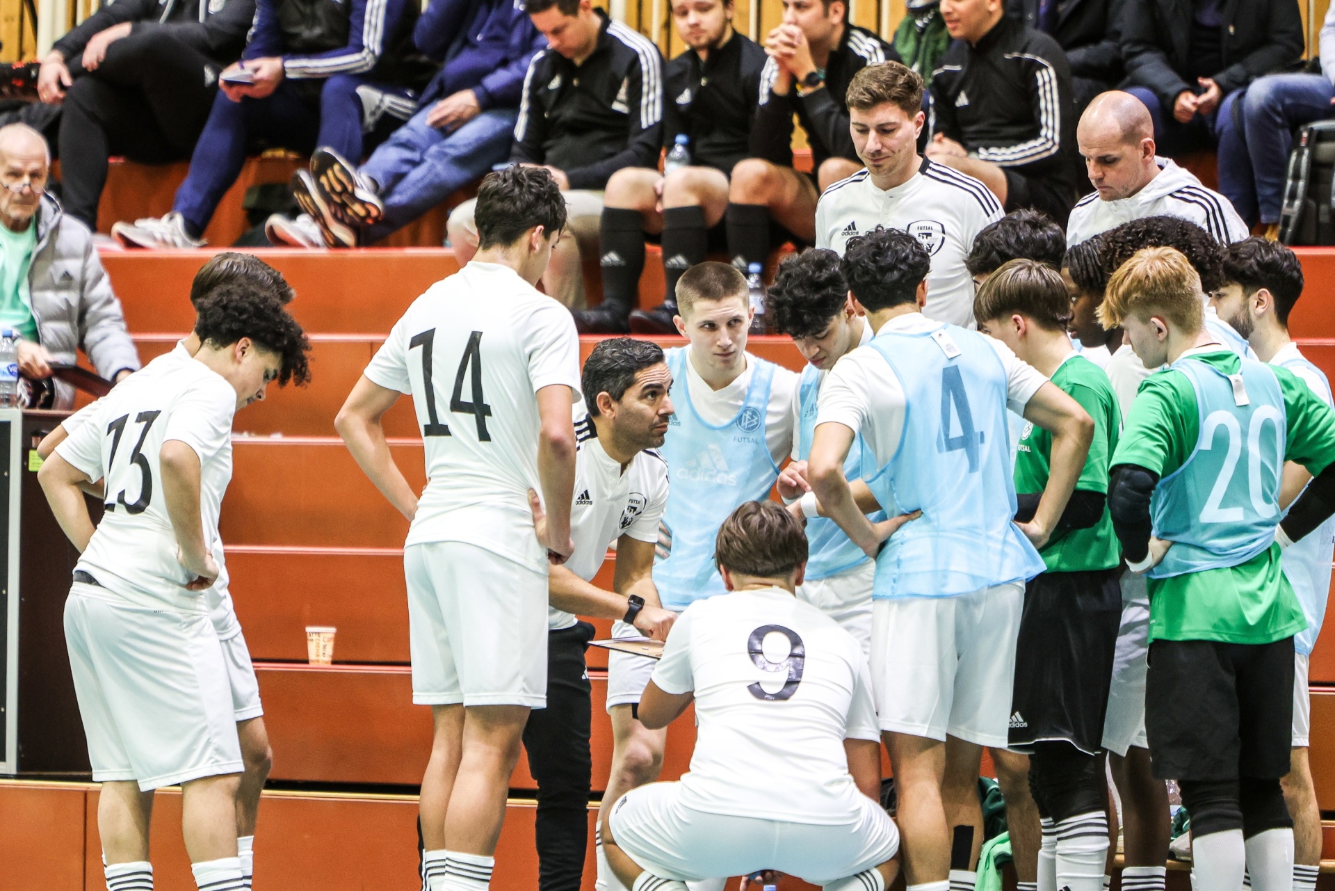 [{"clang_id":1,"value":"Fußballteam in Besprechung am Spielfeldrand. Spieler mit Nummern auf Trikots umringen Trainer, der Handzeichen gibt. Im Hintergrund Zuschauerreihen."}]