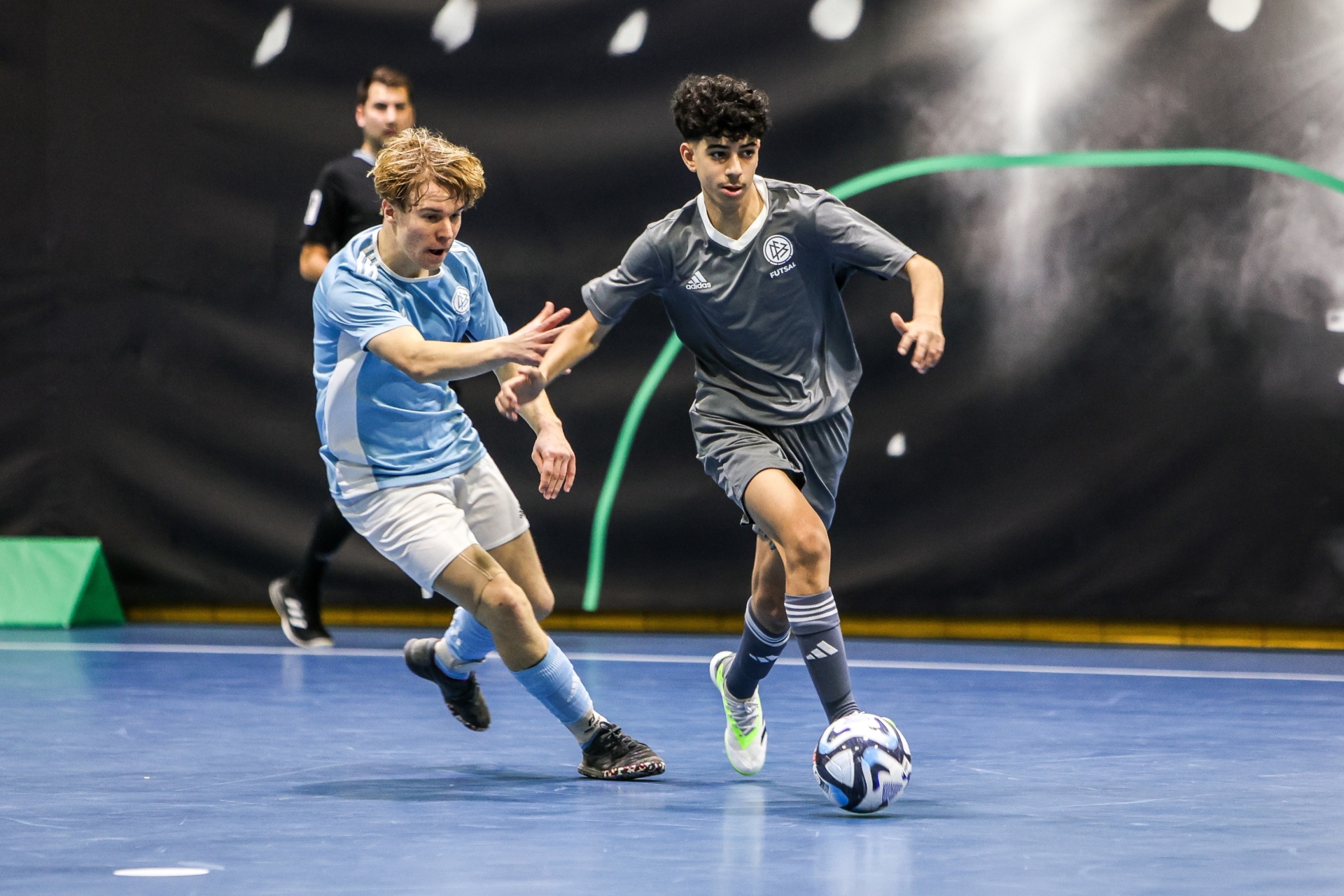 [{"clang_id":1,"value":"Zwei Fußballspieler auf blauem Hallenfußballboden. Ein Spieler in blauem Trikot dribbelt den Ball, ein anderer in hellem Trikot versucht, ihn zu blocken."}]