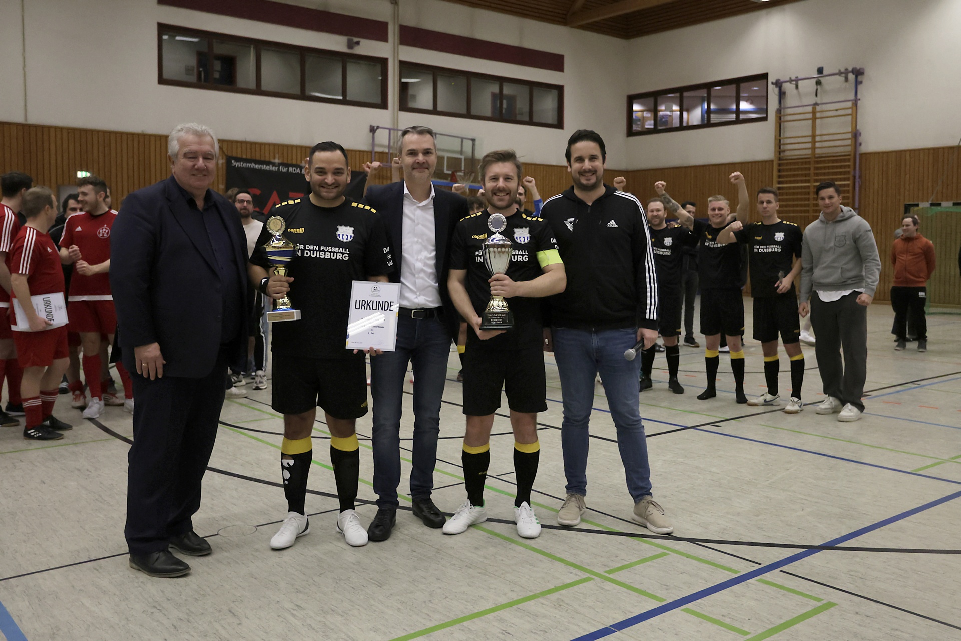 [{"clang_id":1,"value":"Herren stehen in einer Sporthalle. Einige halten Trophäen und Urkunden. Im Hintergrund weitere Personen und eine Wand mit Fenstern."}]