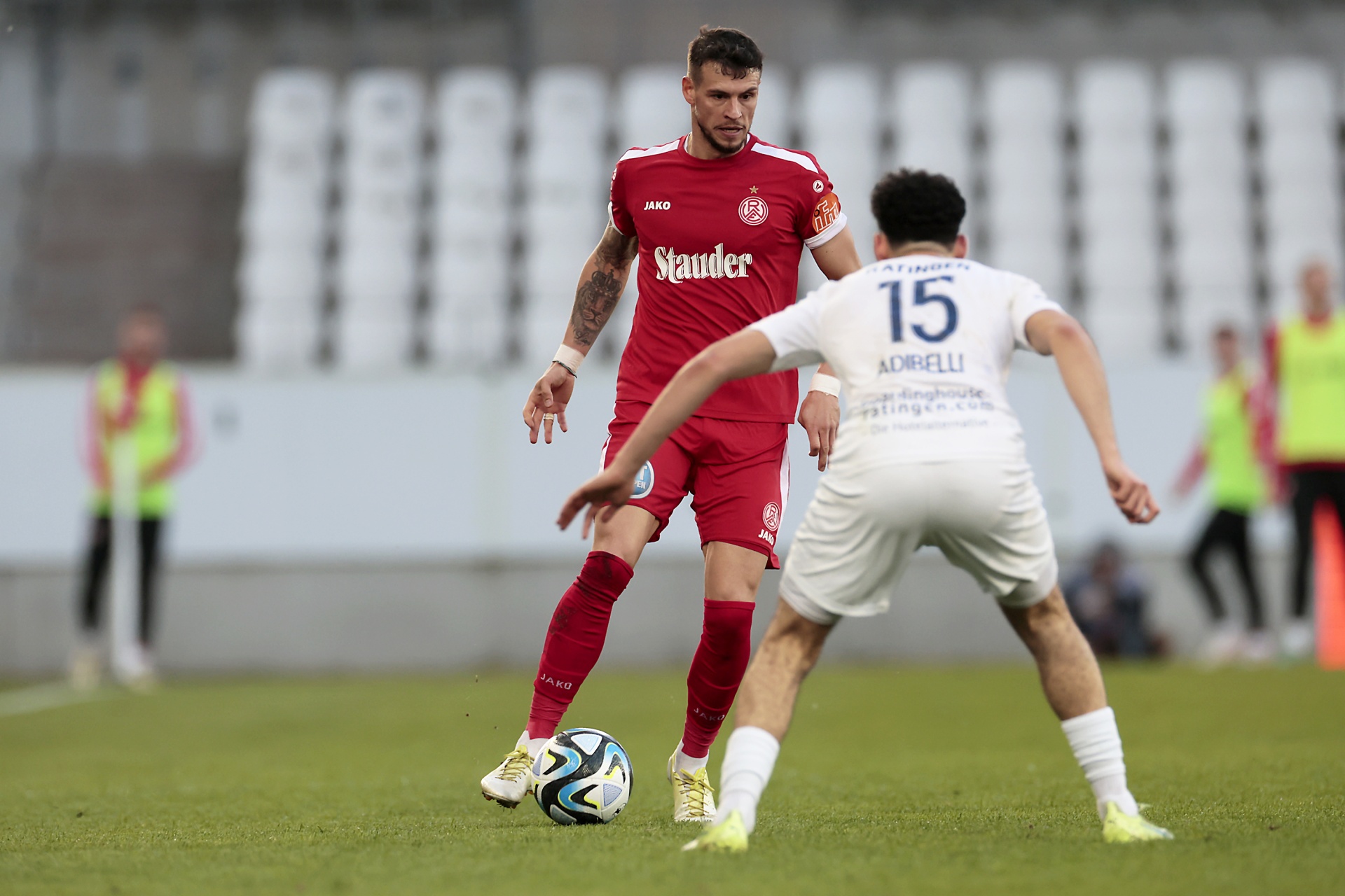 [{"clang_id":1,"value":"Zwei Fußballspieler im Spiel. Ein Spieler in rot-weißer Montur dribbelt den Ball, der andere in Weiß steht ihm gegenüber. Hintergrund: Stadiontribüne."}]