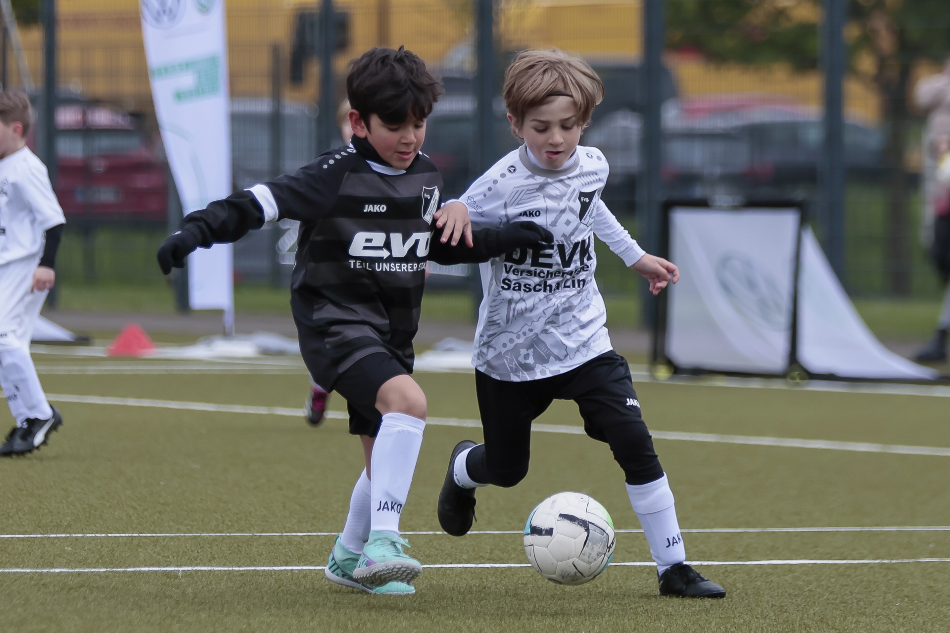 [{"clang_id":1,"value":"Zwei Fußballspieler, Kinder, im Spiel auf grünem Rasen. Dunkles und helles Trikot, kurze Hosen. Ein Kind dribbelt den Ball. Im Hintergrund weitere Spieler und eine Bande."}]
