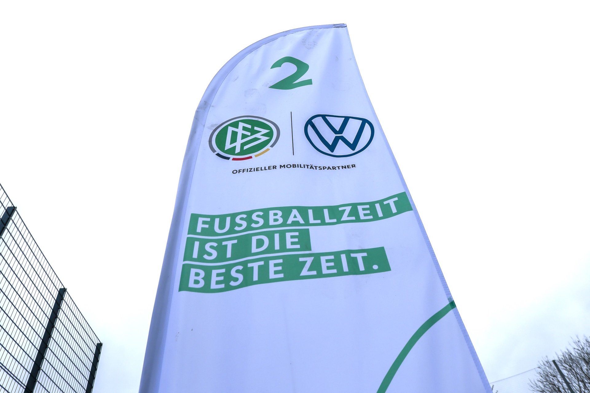 [{"clang_id":1,"value":"Werbeflagge mit den Logos von Borussia Dortmund und Volkswagen. Text: \"FUSSBALLZEIT IST DIE BESTE ZEIT.\". Im Hintergrund ein Zaun und Grünfläche."}]