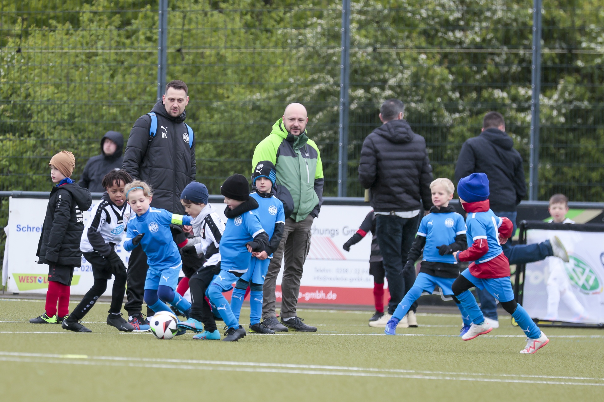 [{"clang_id":1,"value":"Fußballtraining von Kindern: Eine Gruppe kleiner Spieler in blauen Trikots übt auf einem Rasenplatz. Zwei Trainer stehen am Rand. Zuschauer im Hintergrund."}]