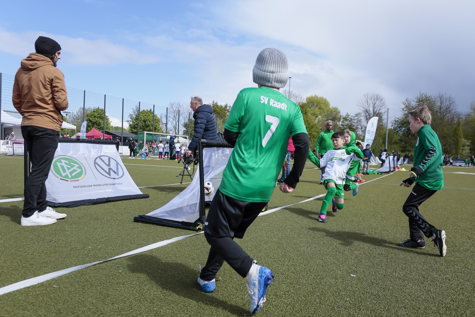 [{"clang_id":1,"value":"Fußballspiel auf Rasenfeld. Kinder in grünen Trikots laufen, ein Mann steht am Spielfeldrand und beobachtet. Im Hintergrund weitere Personen und ein Banner."}]
