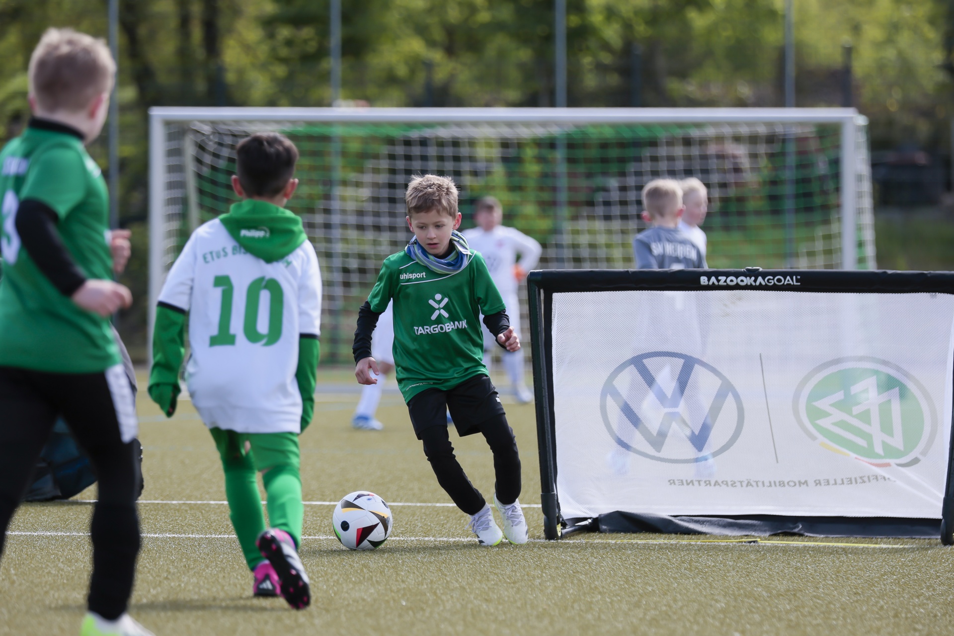 [{"clang_id":1,"value":"Fußballtraining: Junge mit grünem Trikot dribbelt Ball an einem kleinen Tor, weitere Kinder im Hintergrund auf dem Rasen."}]