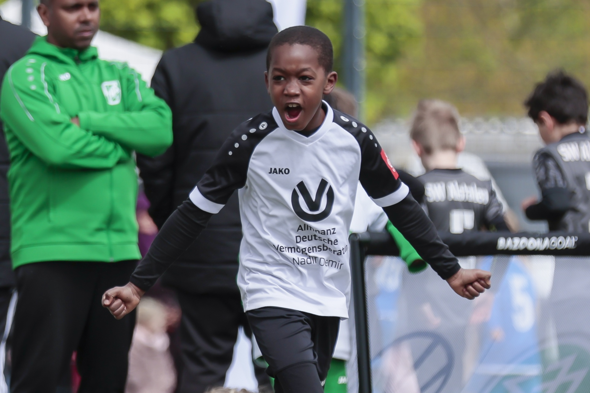 [{"clang_id":1,"value":"Junge Fußballspieler jubelt mit erhobenen Armen auf dem Spielfeld. Im Hintergrund weitere Spieler und Zuschauer."}]