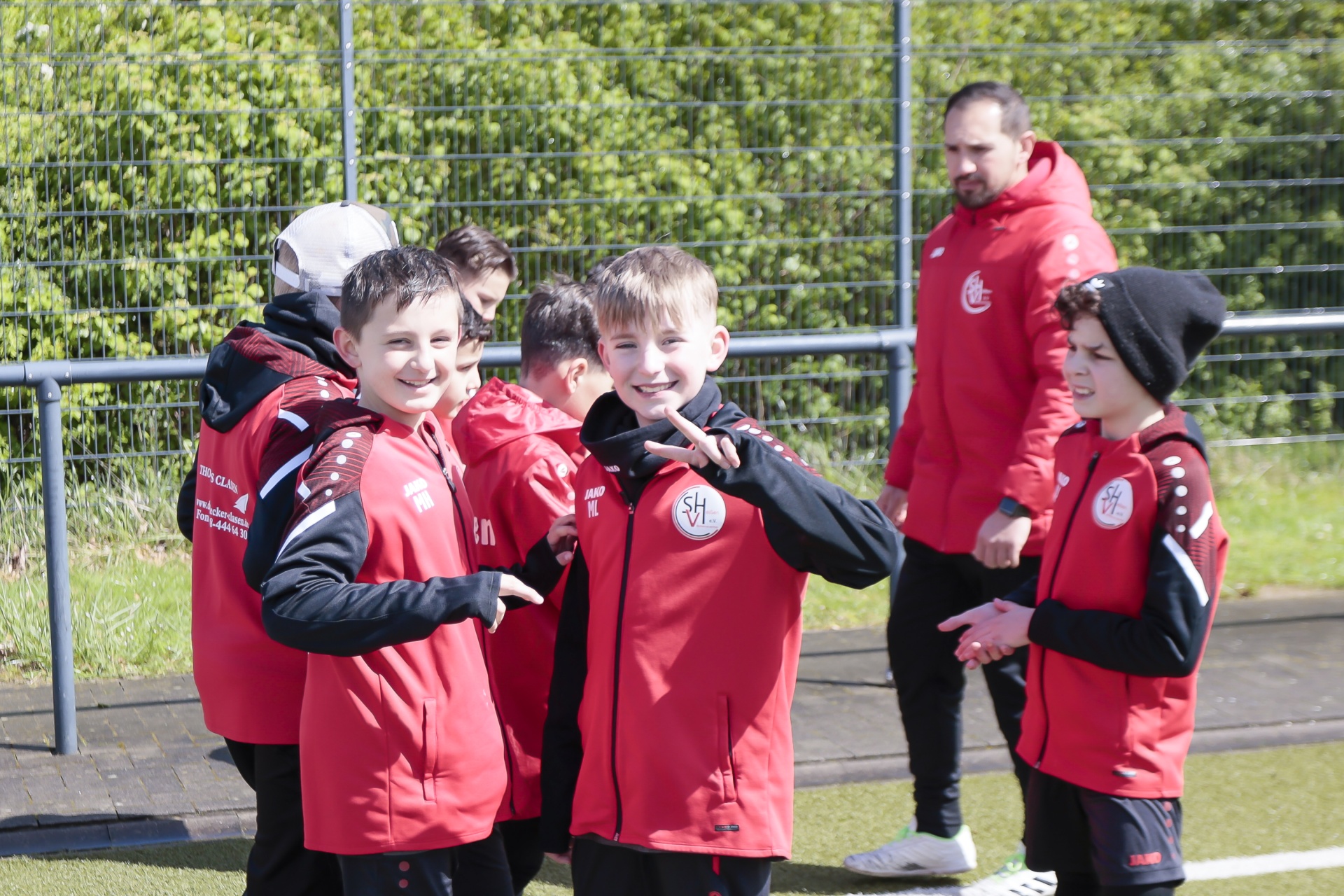 [{"clang_id":1,"value":"Fußballjugendliche in roten Trainingsanzügen feiern auf einem Fußballfeld. Ein Trainer steht daneben. Im Hintergrund grüne Hecken."}]