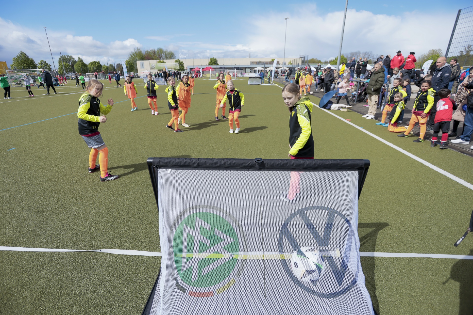 [{"clang_id":1,"value":"Fußballtraining mit Kindern auf Kunstrasenplatz. Im Vordergrund ein Fußballtor mit VW-Logo und grünem Schild. Mehrere Kinder in Sportkleidung üben Schüsse."}]