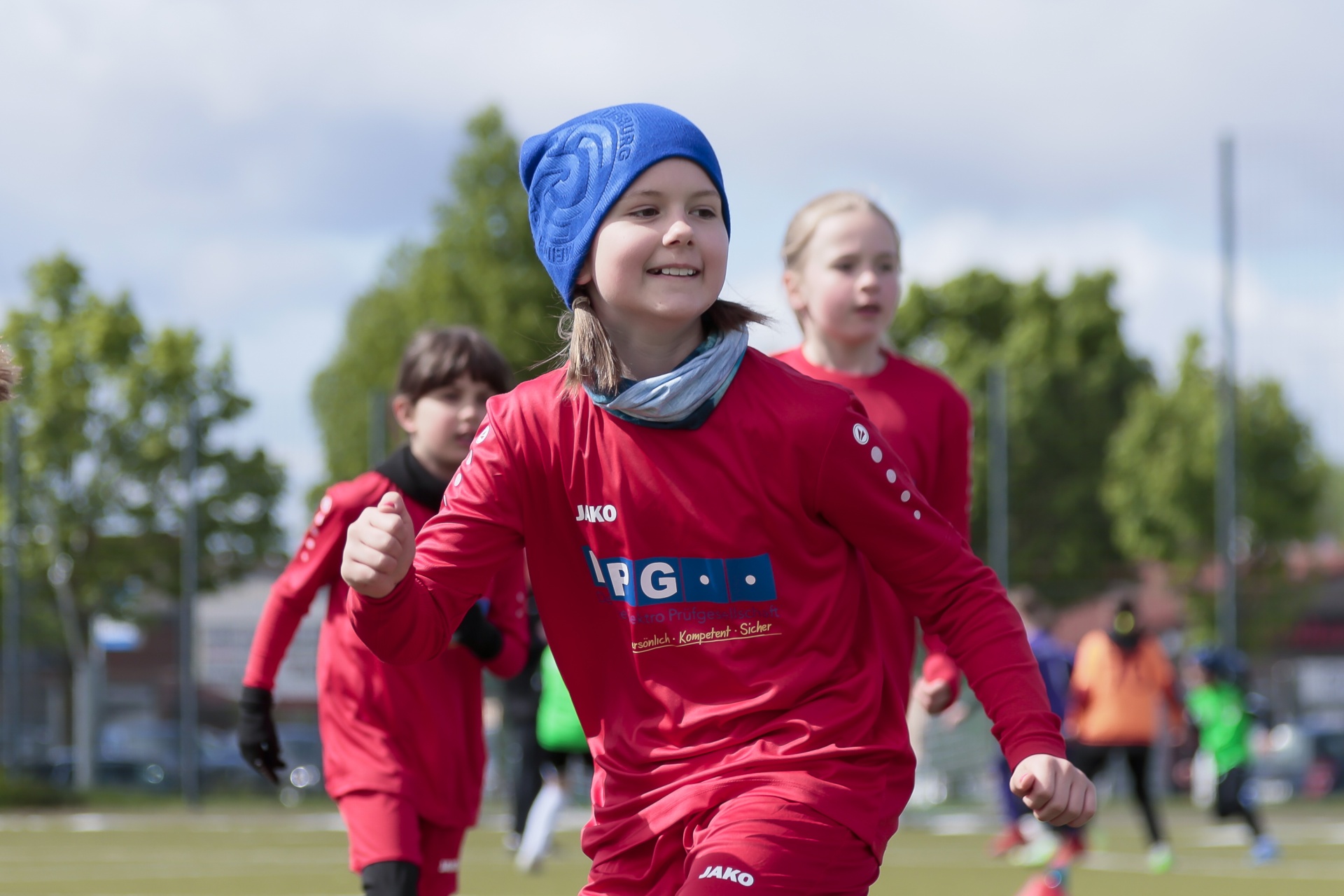 [{"clang_id":1,"value":"Jungen-Fußballmannschaft im roten Trikot auf grünem Rasen. Vordergrund: Lächelndes Mädchen mit blauer Mütze. Hintergrund: Weitere Spieler und Bäume."}]