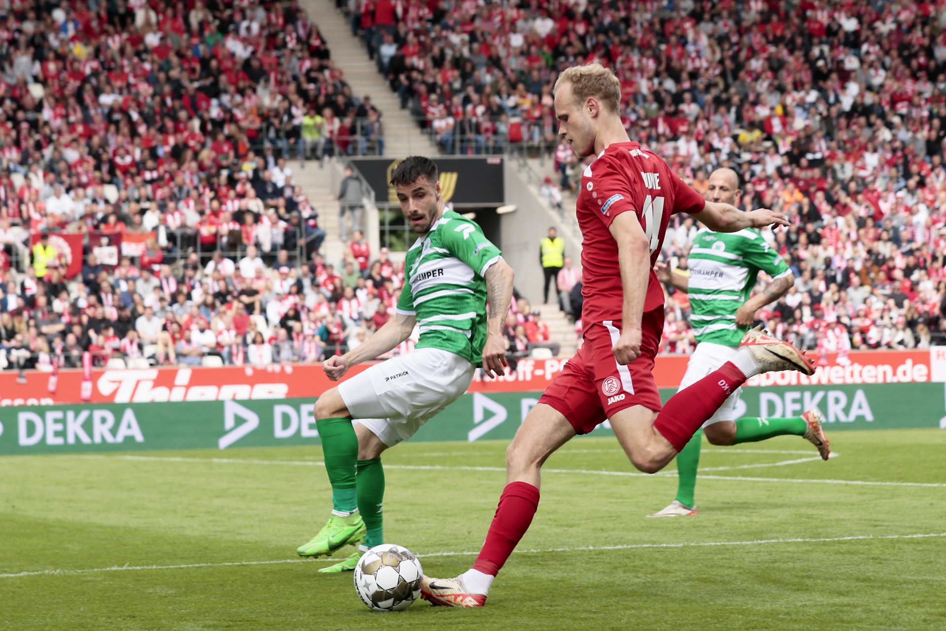 [{"clang_id":1,"value":"Zwei Fußballspieler im Wettkampf. Links Spieler in grünen Trikots, rechts Spieler in roten Trikots. Hintergrund: Stadion mit Zuschauern."}]