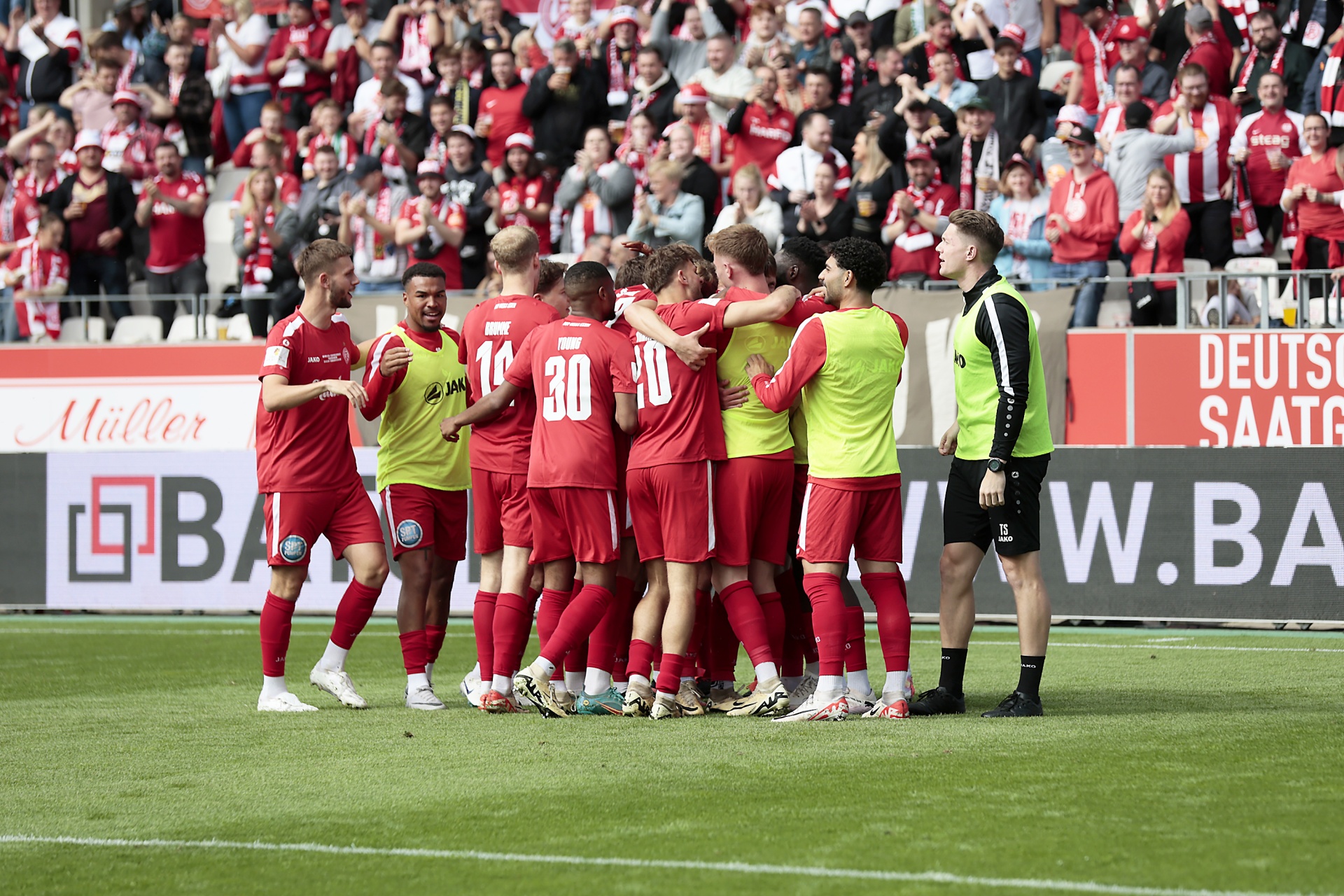 [{"clang_id":1,"value":"Fußballspieler in roten Trikots feiern ein Tor inmitten eines jubelnden Publikums im Stadion. Ein Schiedsrichter steht daneben. Rasenfläche im Vordergrund."}]