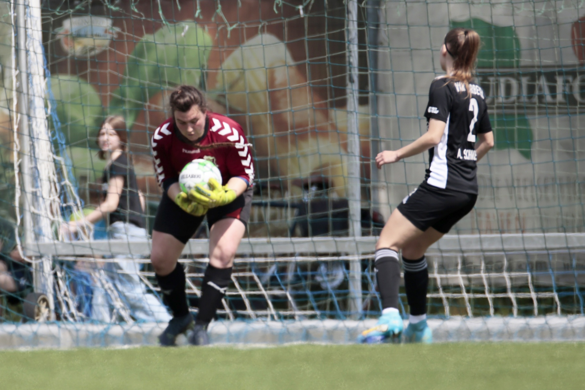 [{"clang_id":1,"value":"Fußballspiel: Torwartin in schwarzer Ausrüstung springt, um Ball zu halten. Spieler mit Nummer 2 schießt aufs Tor. Im Hintergrund Zuschauer und Banner."}]