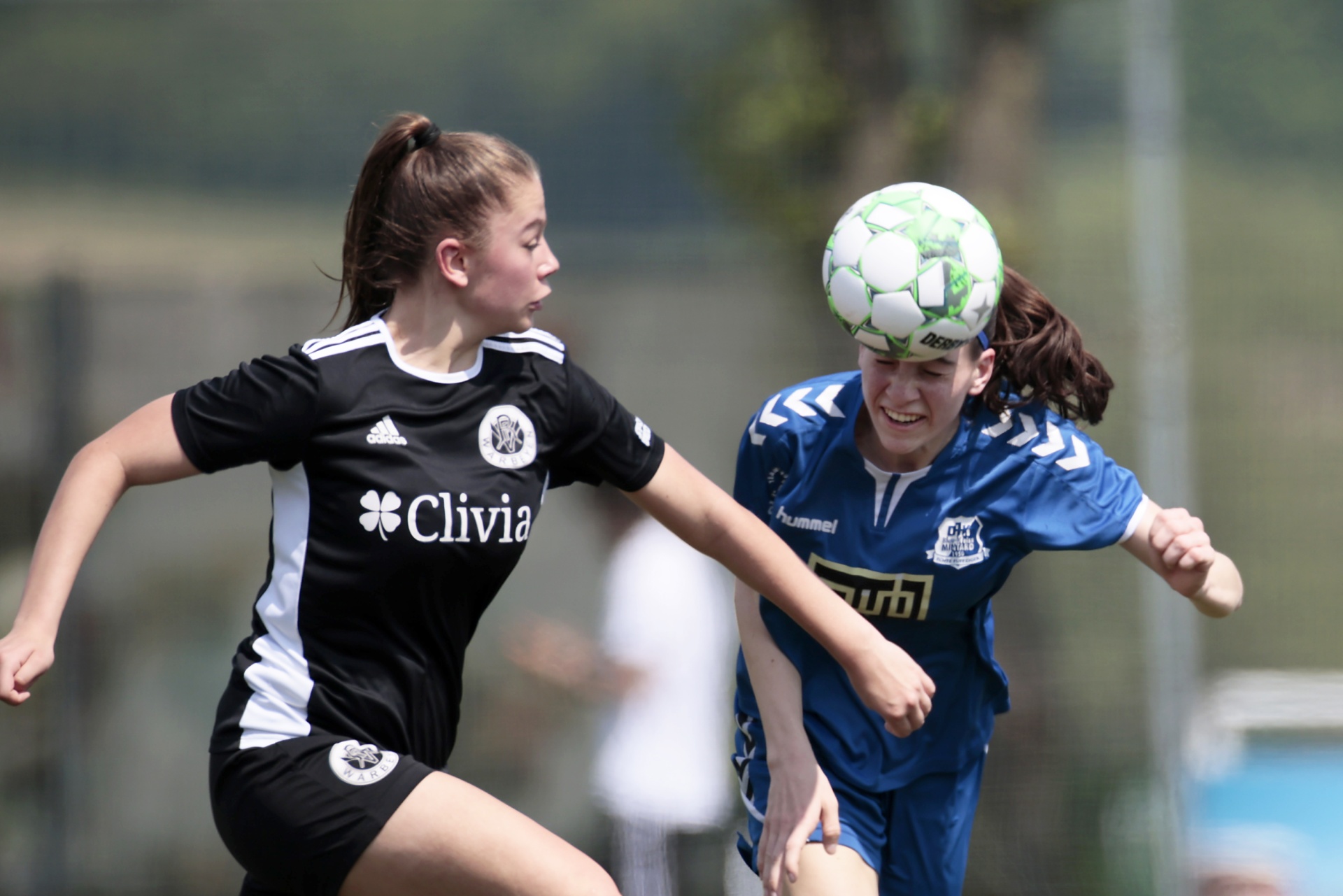 [{"clang_id":1,"value":"Zwei Fußballspielerinnen im Spiel. Links trägt eine Spielerin ein schwarzes Trikot, rechts ein blaues. Die rechte Spielerin köpft den Ball."}]
