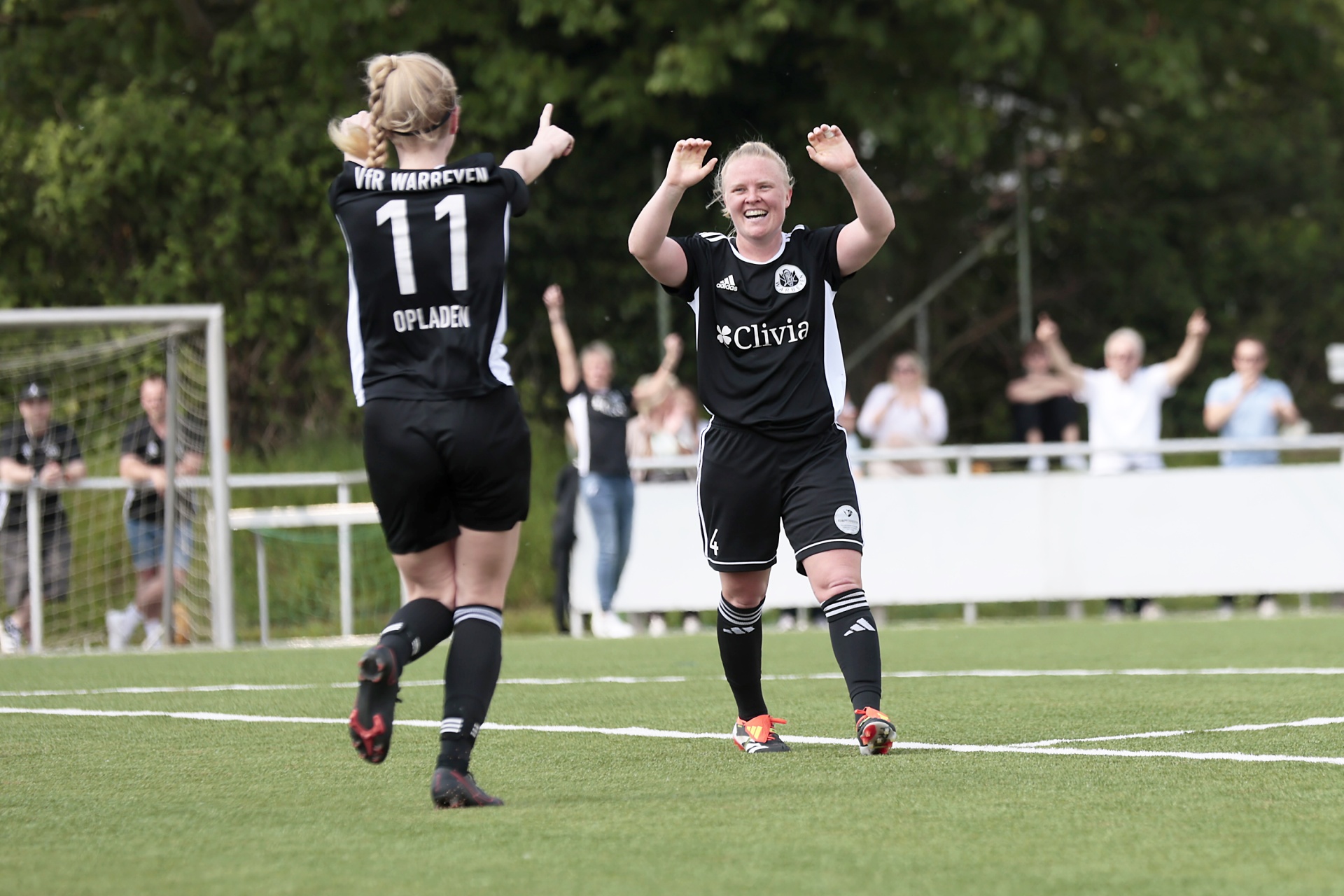 [{"clang_id":1,"value":"Zwei Fußballspielerinnen jubeln auf einem grünen Rasenfeld. Im Hintergrund Zuschauer und Baumreihe. Die Spielerinnen tragen schwarz-weiße Trikots."}]