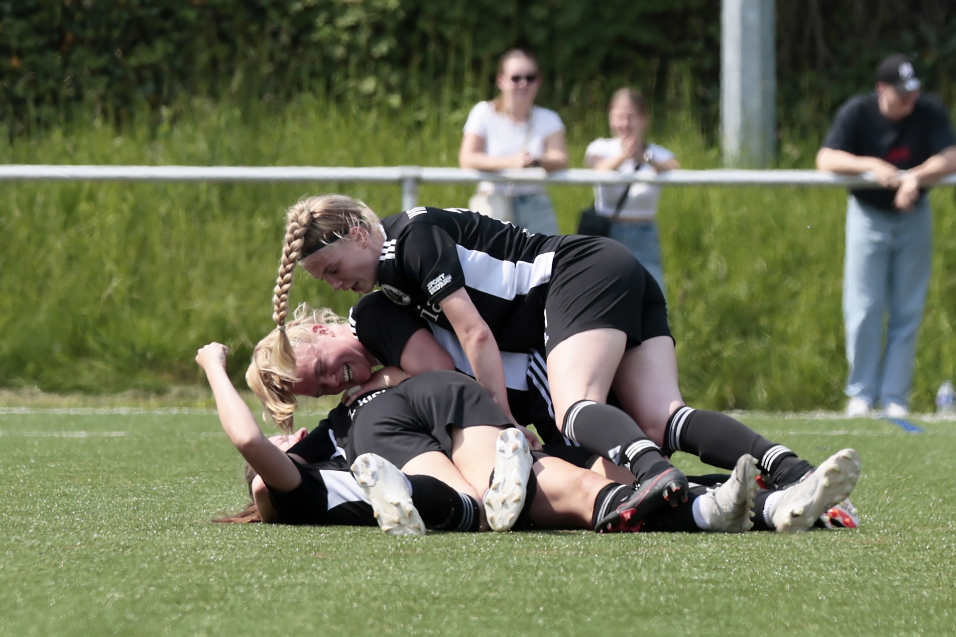 [{"clang_id":1,"value":"Rugby-Spielerinnen kämpfen am Boden um den Ball auf grünem Rasen. Zuschauer stehen im Hintergrund hinter einer Barriere."}]