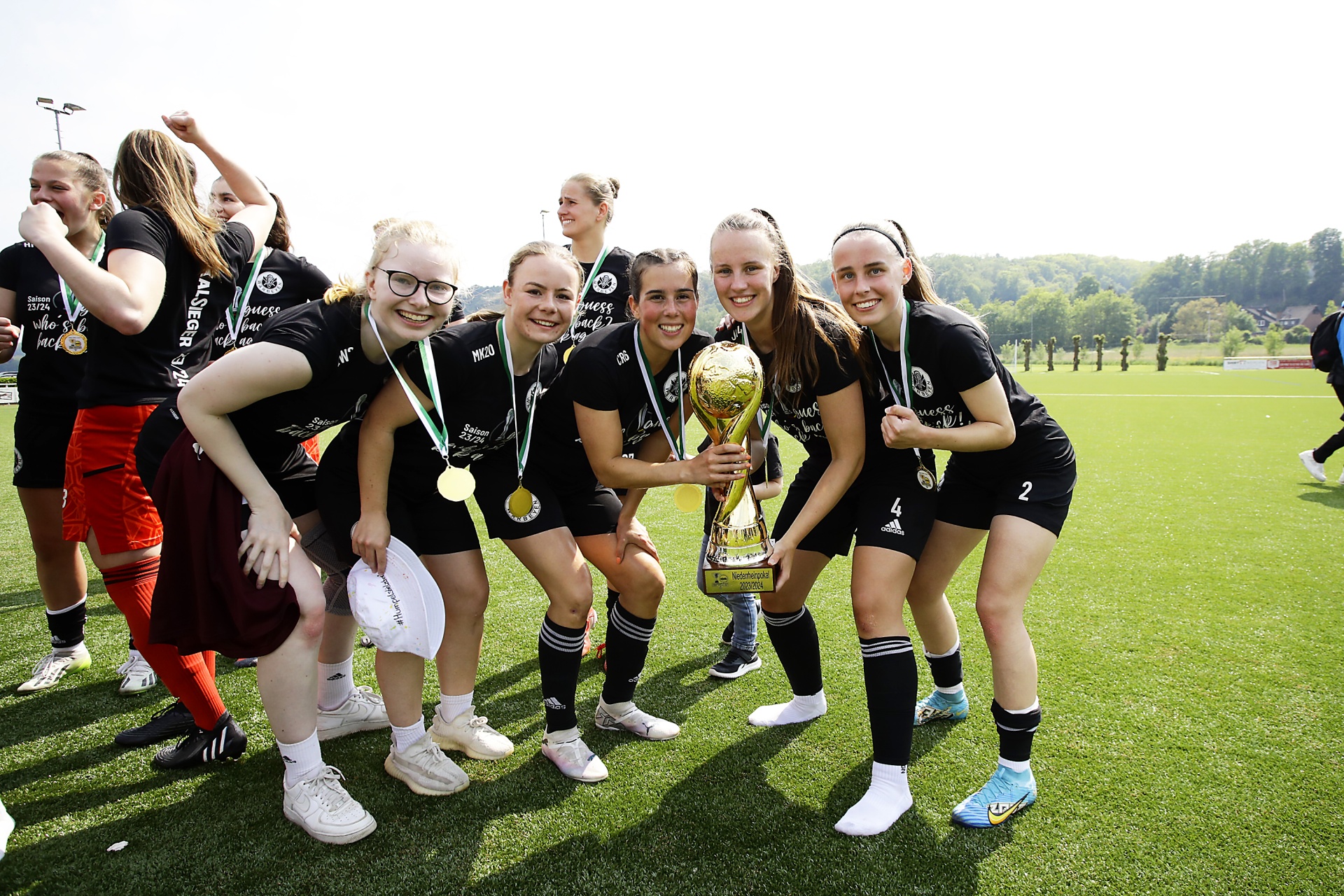 [{"clang_id":1,"value":"Fußballteam mit Medaillen und Pokal auf Rasenfeld. Die Spielerinnen lächeln und posieren für das Foto."}]